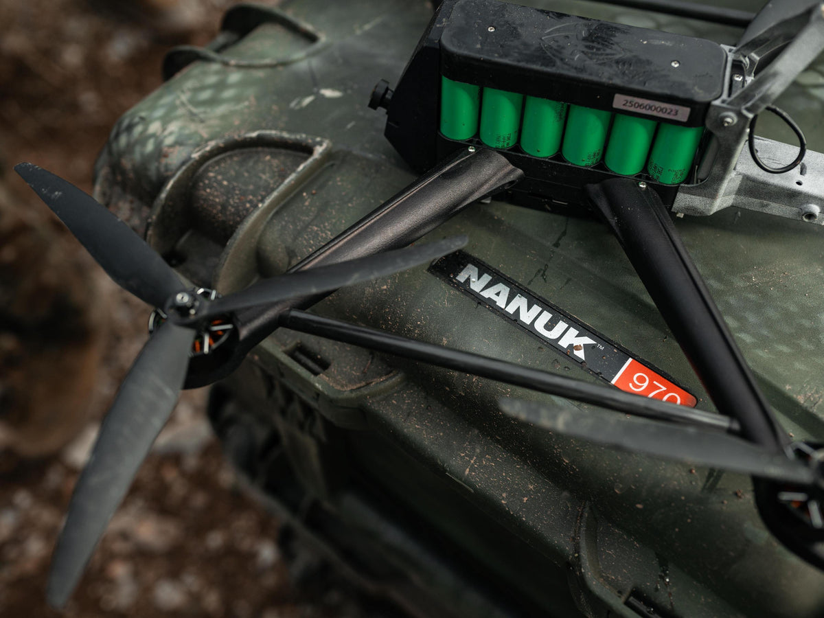 Close-up of a black Nanuk 970 quadcopter drone resting on a camouflage military-style vehicle in an outdoor setting.