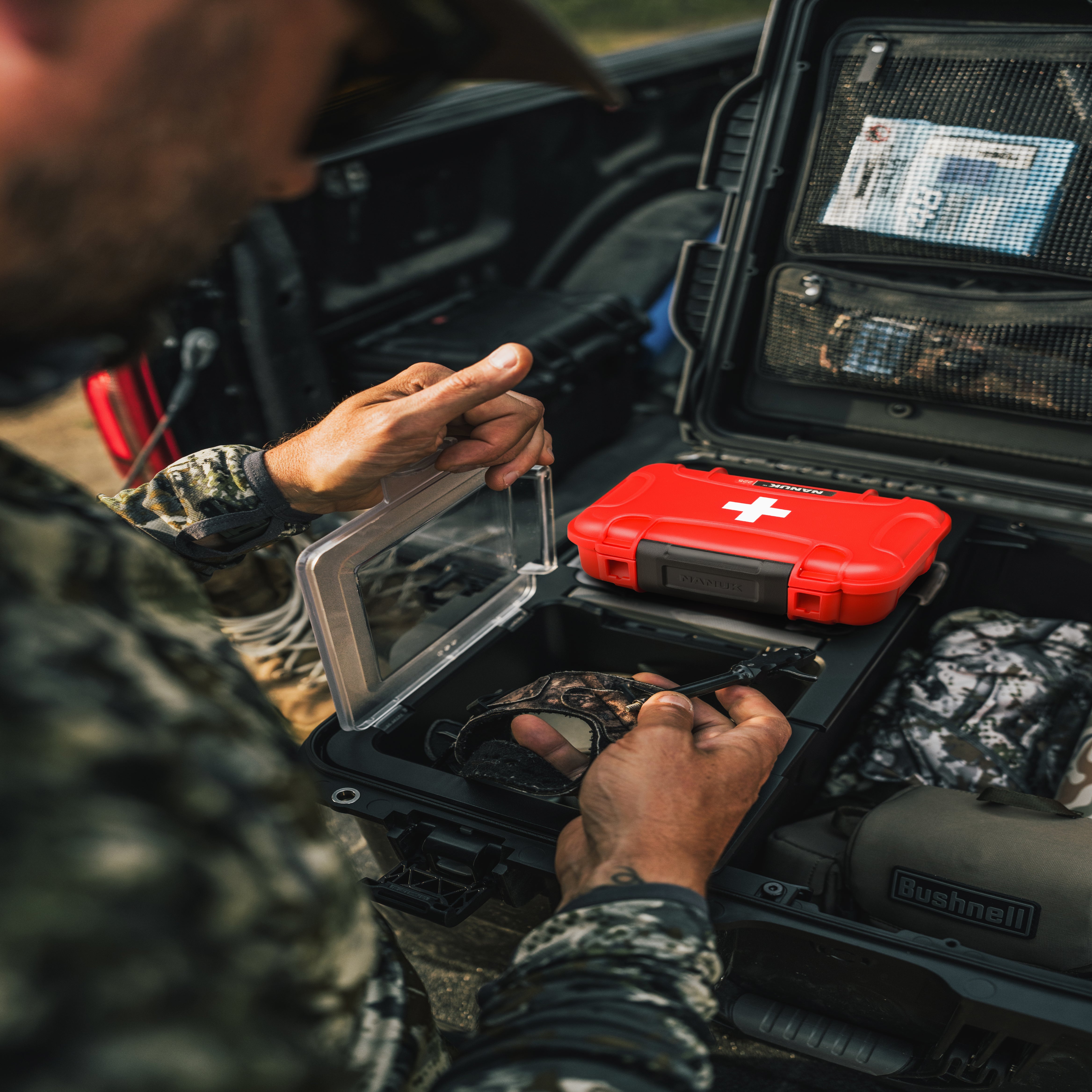 Person organizing items in a black case with a red first aid kit inside, wearing camouflage clothing. Person organizing items in a black case with a red first aid kit inside, wearing camouflage clothing.