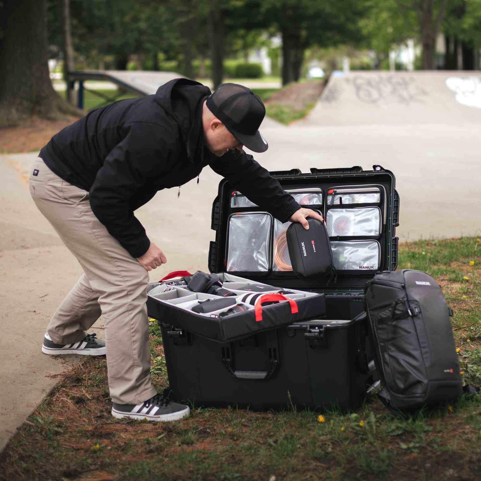 Person organizing equipment in a large black suitcase outdoors.