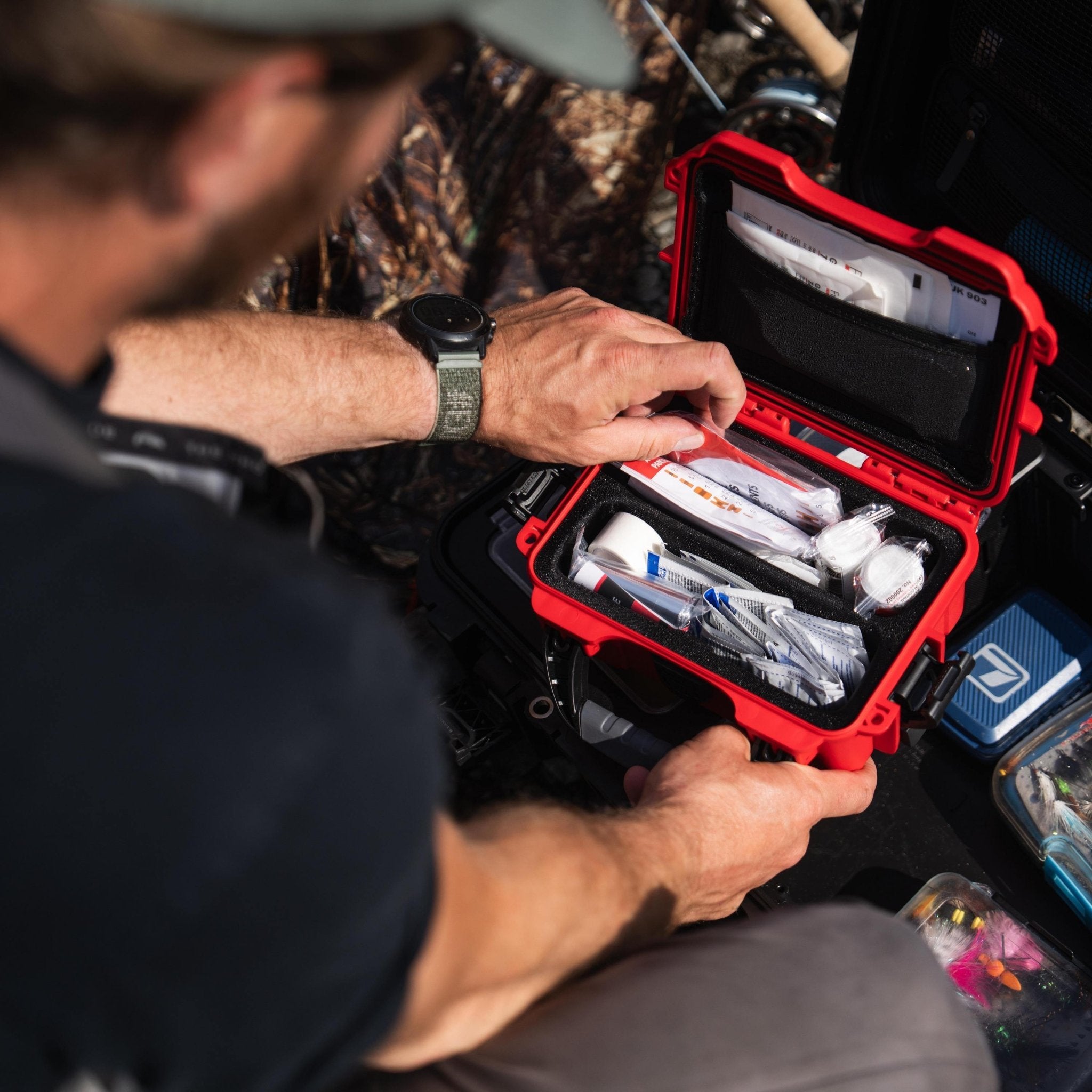 Person organizing items in a red and black case outdoors