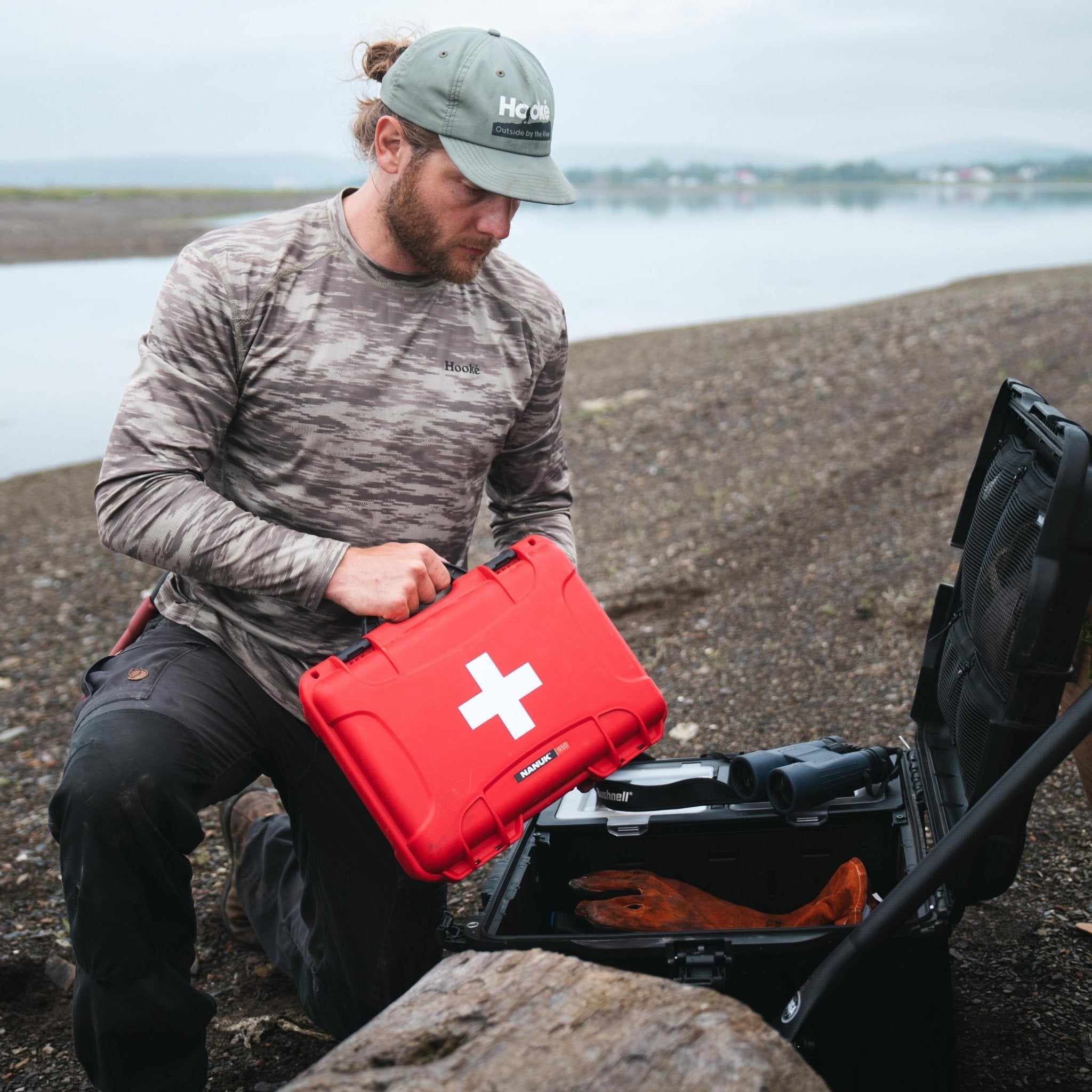 Man holding a red first aid case by a body of water Man holding a red first aid case by a body of water