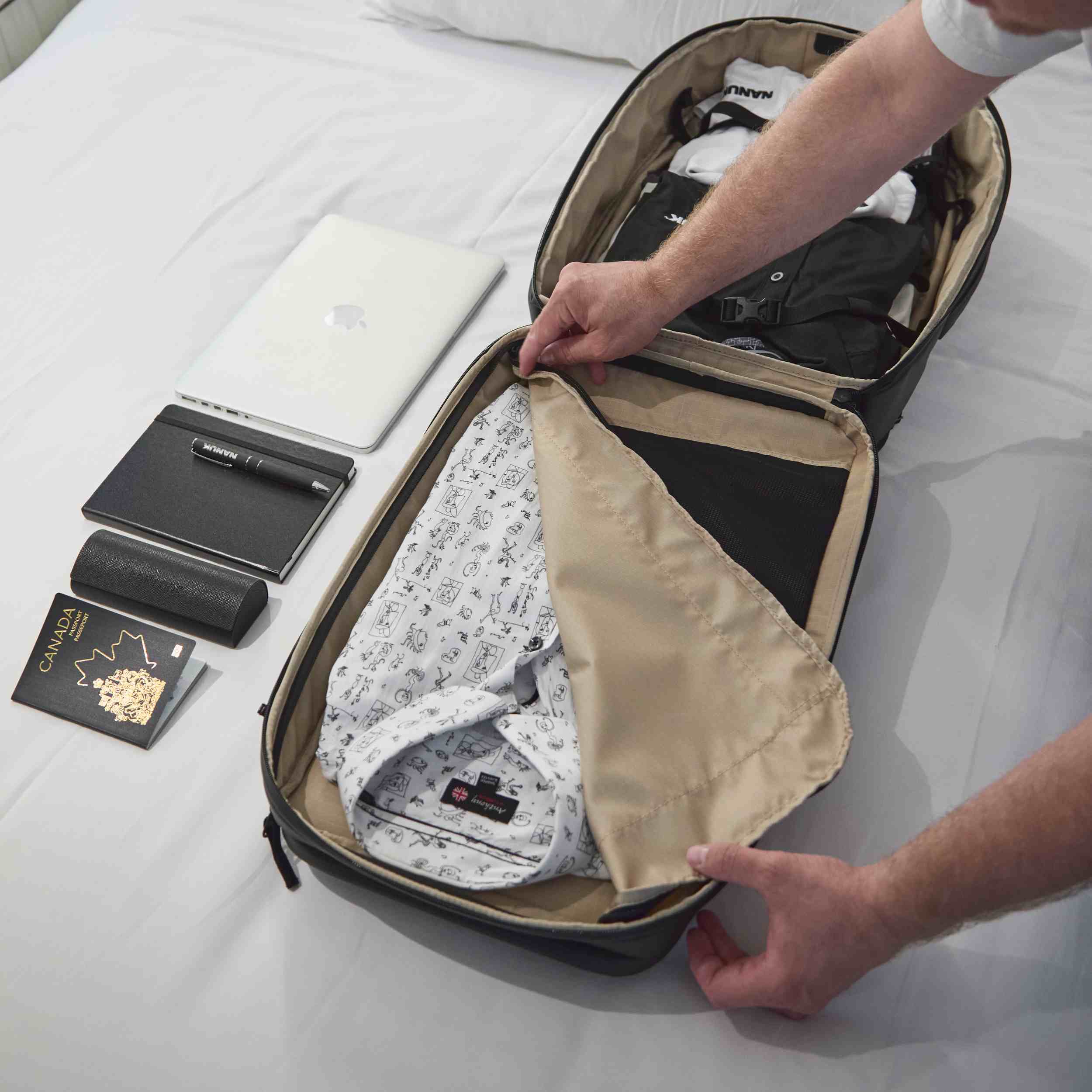 Person packing clothes into a suitcase on a bed with a laptop and other items nearby. Person packing clothes into a suitcase on a bed with a laptop and other items nearby.