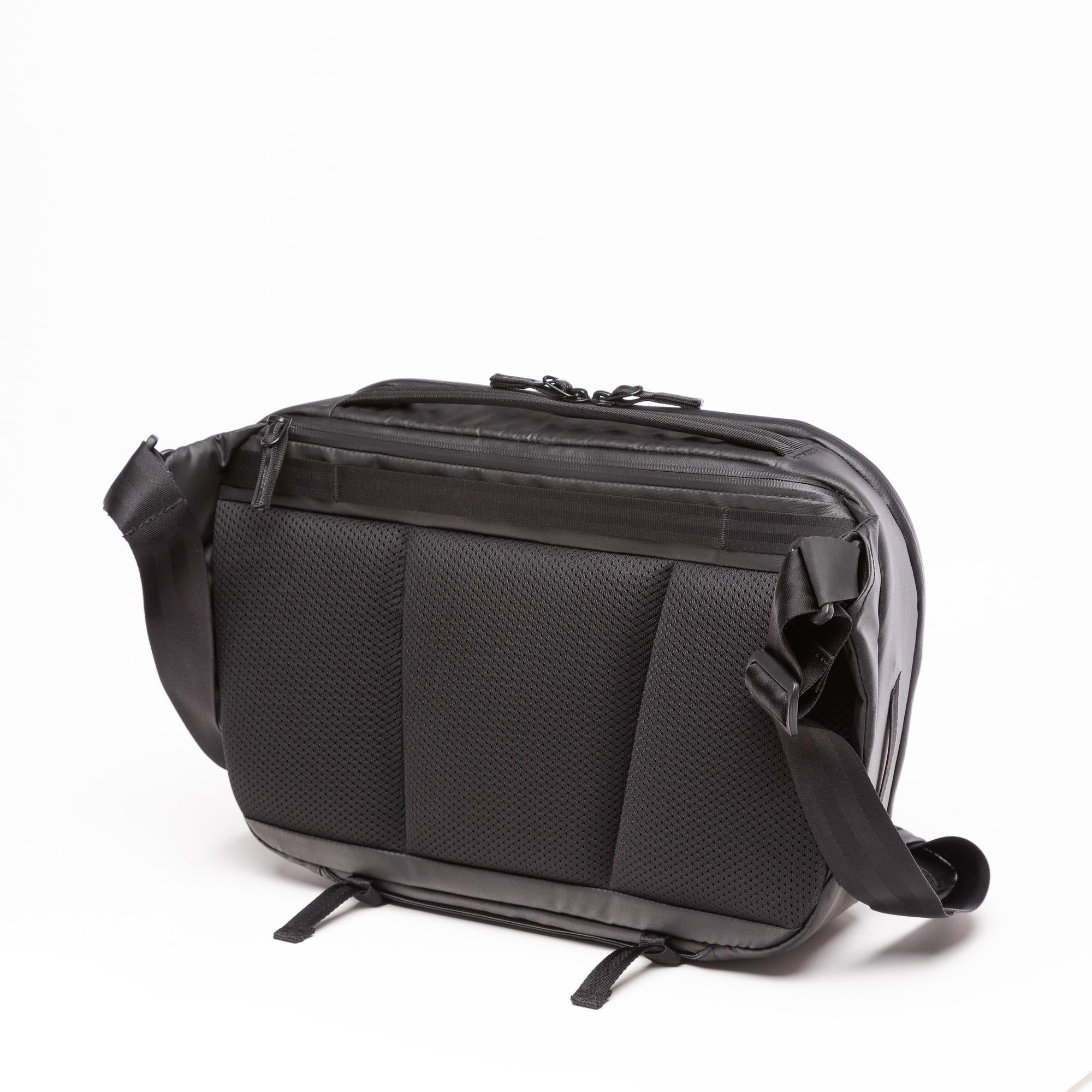 A black crossbody bag with a textured honeycomb pattern on the front pocket, a top zippered compartment, and an adjustable shoulder strap, shown on a white background. A black crossbody bag with a textured honeycomb pattern on the front pocket, a top zippered compartment, and an adjustable shoulder strap, shown on a white background.