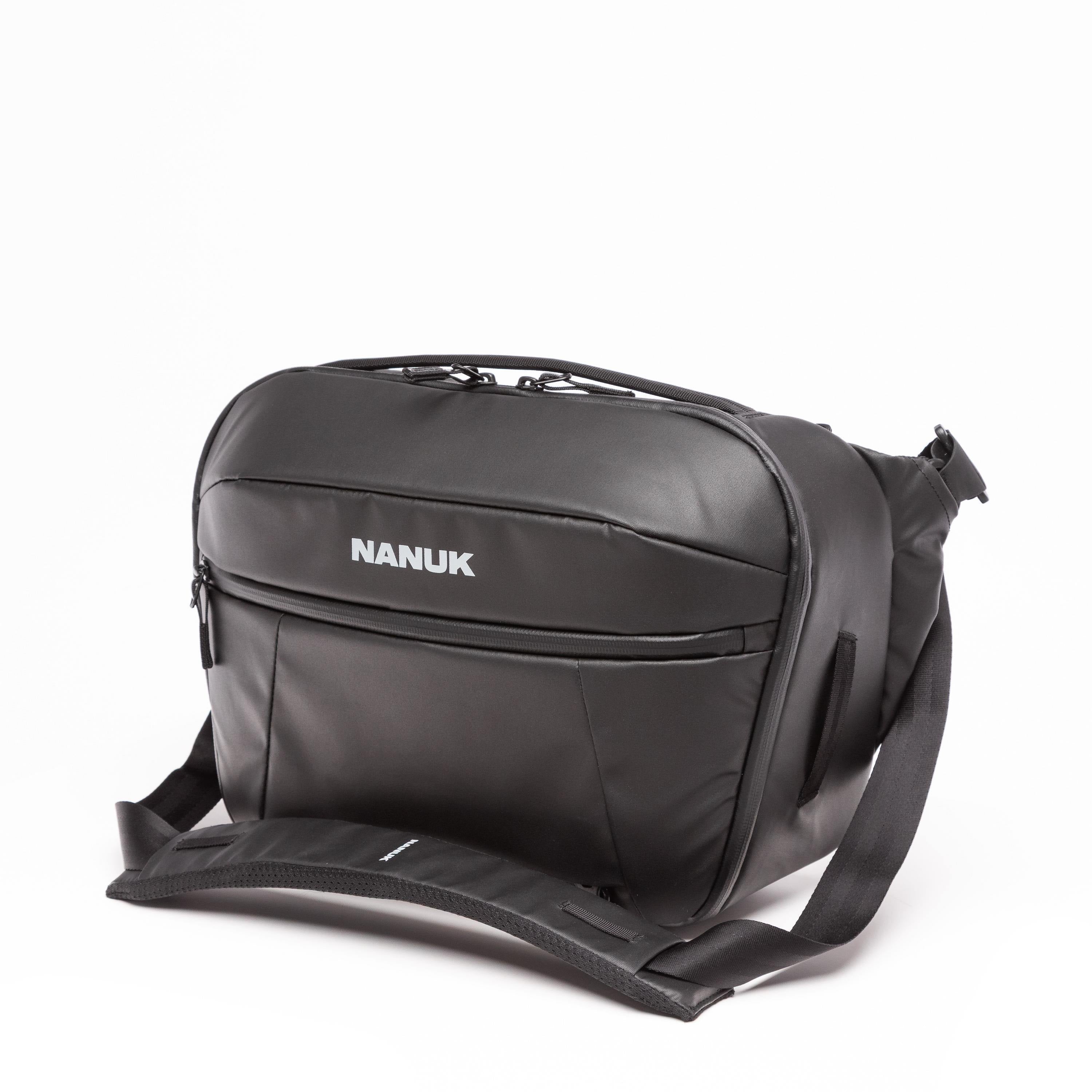 A black Nanuk messenger bag with a white brand logo, shown on a clean white background with its detachable shoulder strap extended. A black Nanuk messenger bag with a white brand logo, shown on a clean white background with its detachable shoulder strap extended.