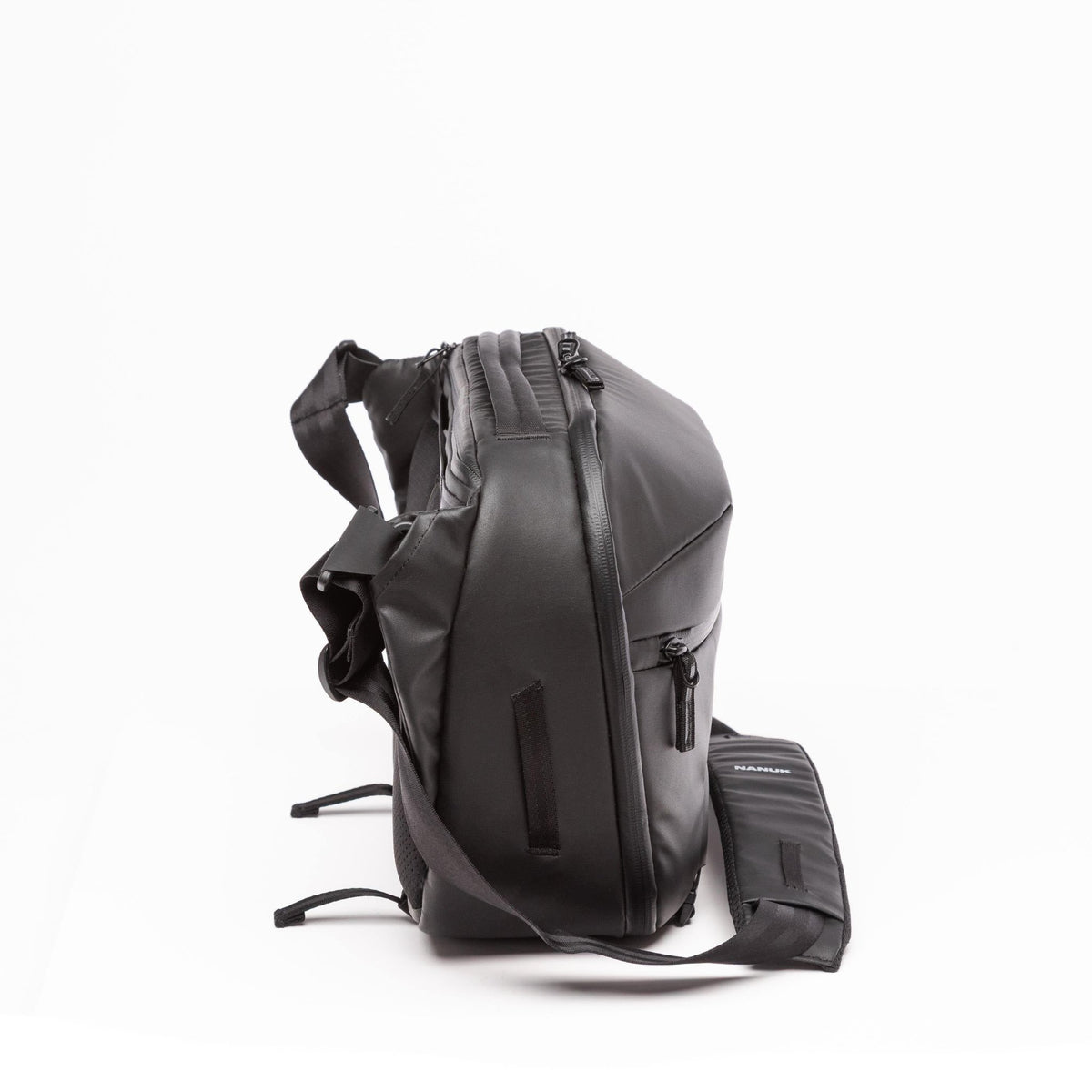 A black backpack with an attached matching pouch, shown from a side profile view on a clean white background. A black backpack with an attached matching pouch, shown from a side profile view on a clean white background.