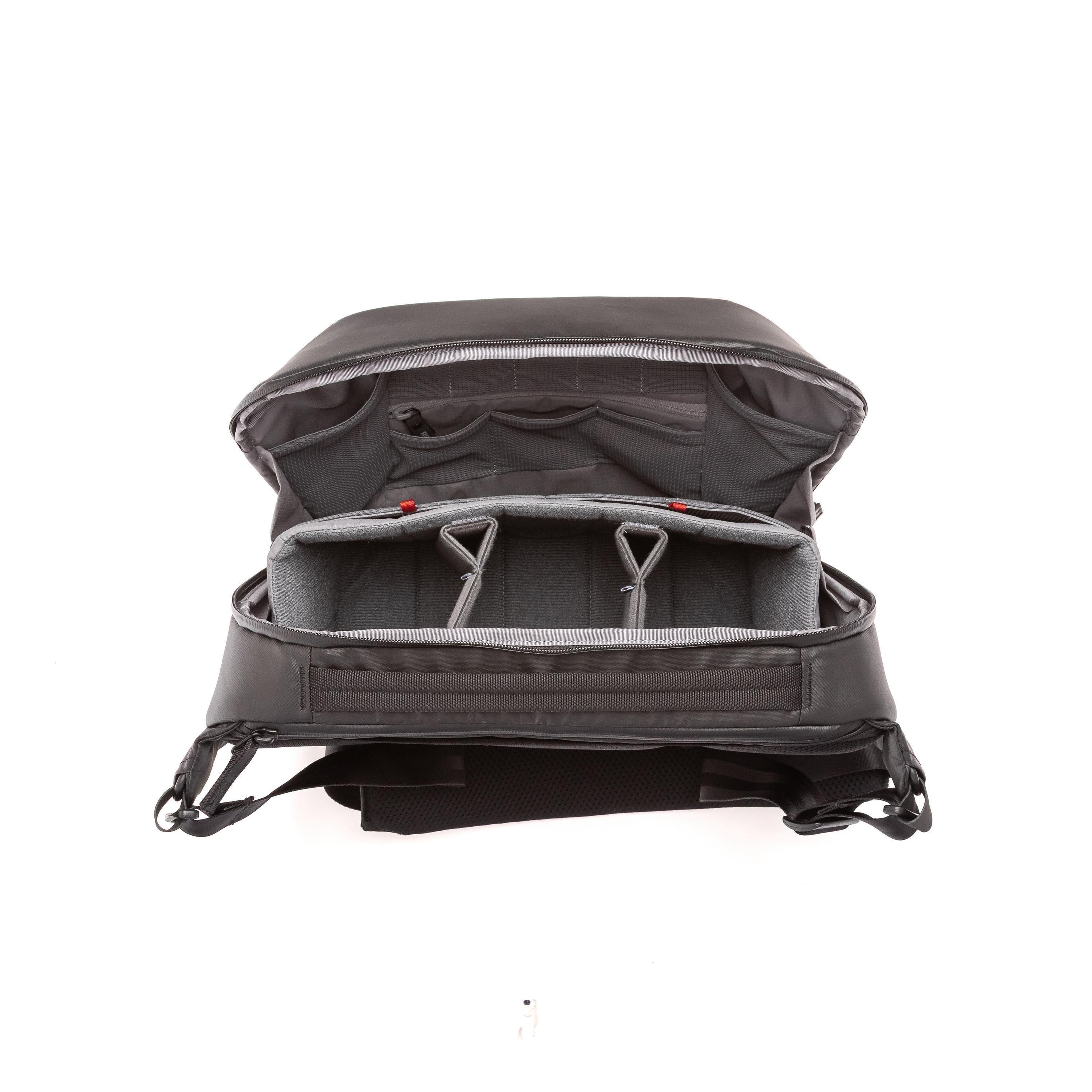 An open black camera backpack shown from the front, displaying its padded interior compartments, foam inserts, and adjustable shoulder straps against a white background. An open black camera backpack shown from the front, displaying its padded interior compartments, foam inserts, and adjustable shoulder straps against a white background.