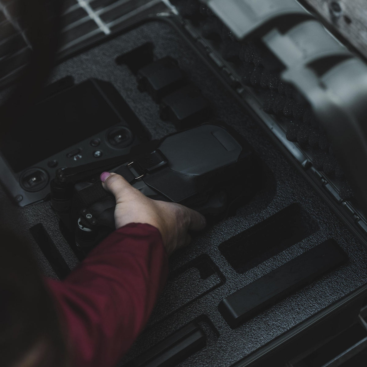 A close-up shot of a person's hand with pink nail polish placing a black drone controller into a custom foam organizer inside a hard protective case.