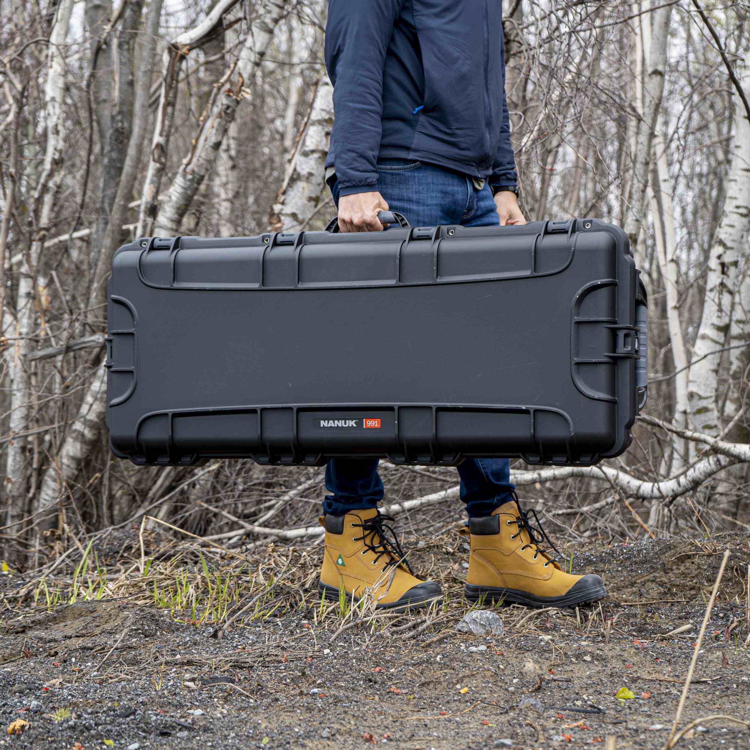 Person holding a large black hard-shell case in a forest setting Person holding a large black hard-shell case in a forest setting