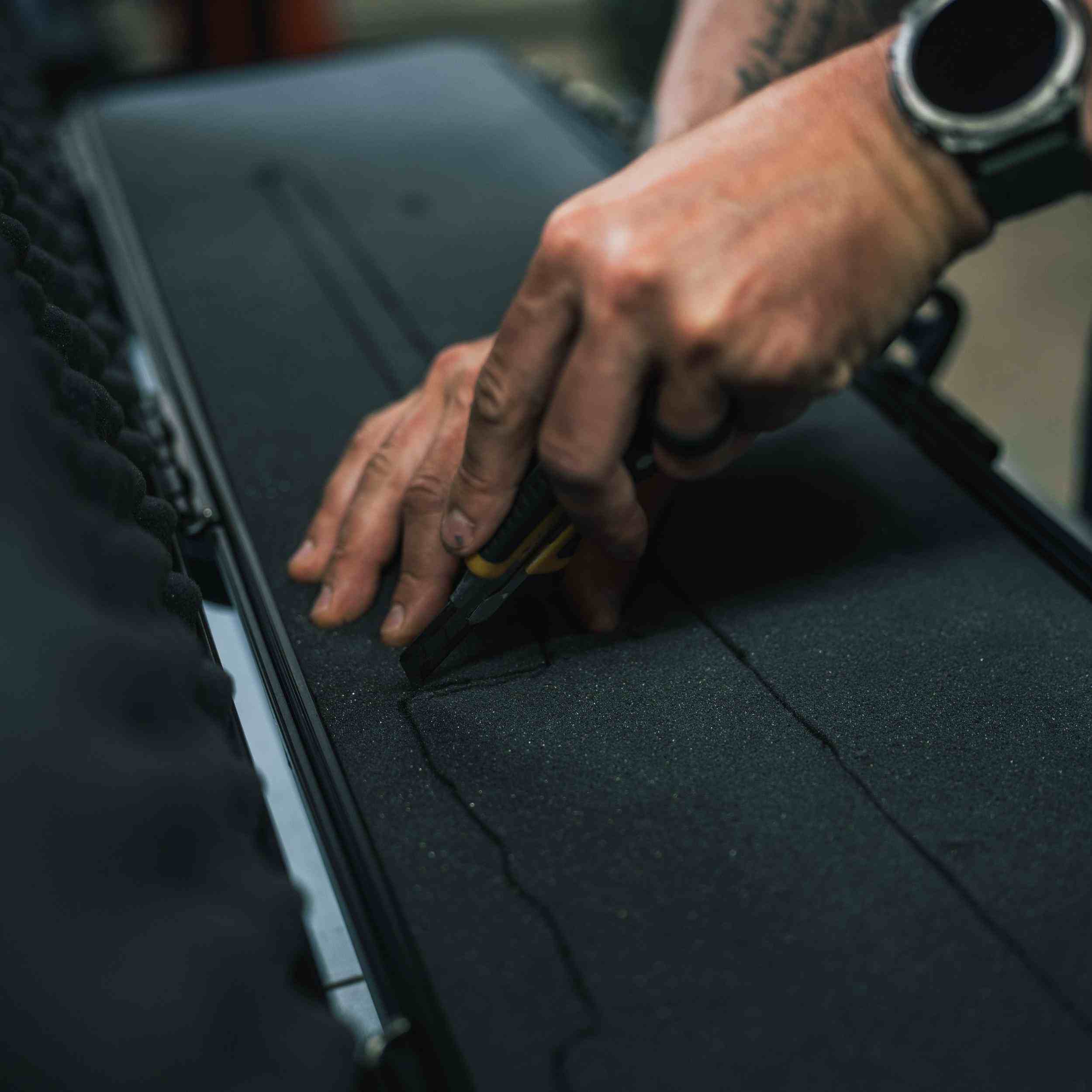 Person using a tool on a black surface with tattoos visible on hands Person using a tool on a black surface with tattoos visible on hands