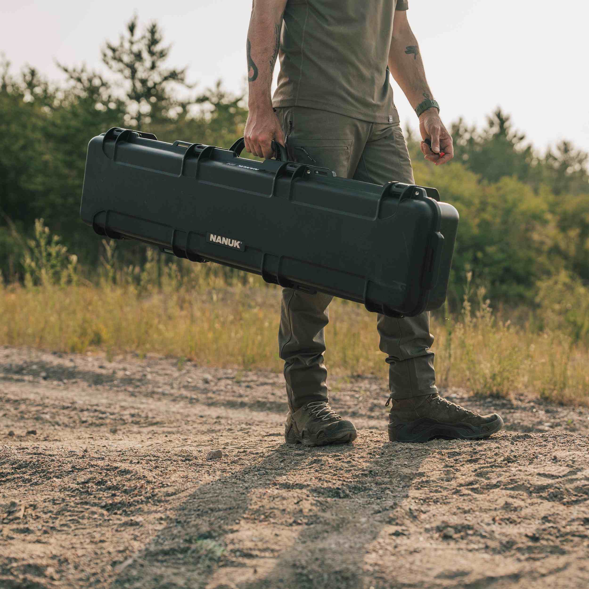Person holding a large black case with 'Nanuk' branding in an outdoor setting. Person holding a large black case with 'Nanuk' branding in an outdoor setting.