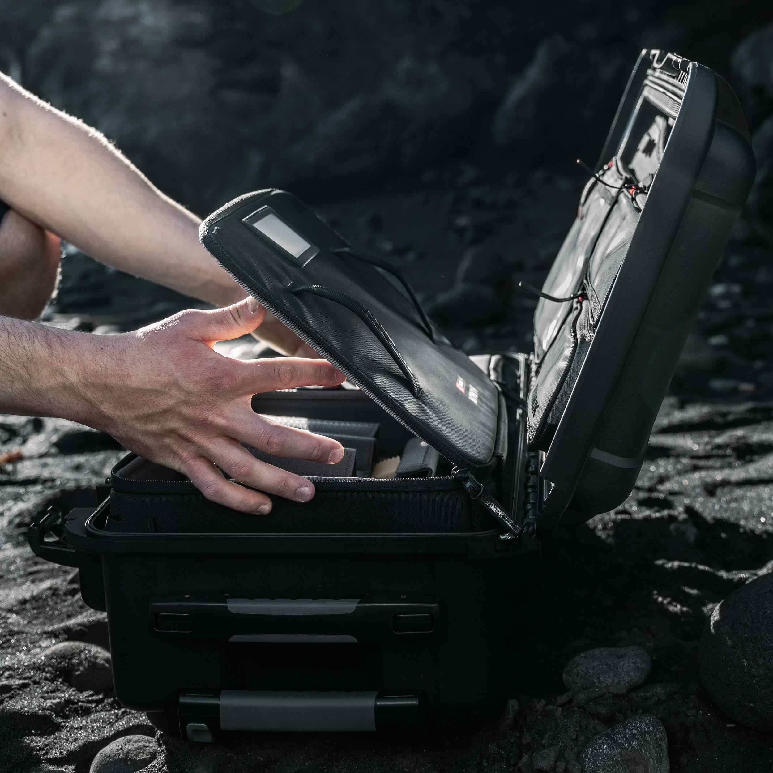 Person opening a black suitcase on a rocky surface Person opening a black suitcase on a rocky surface