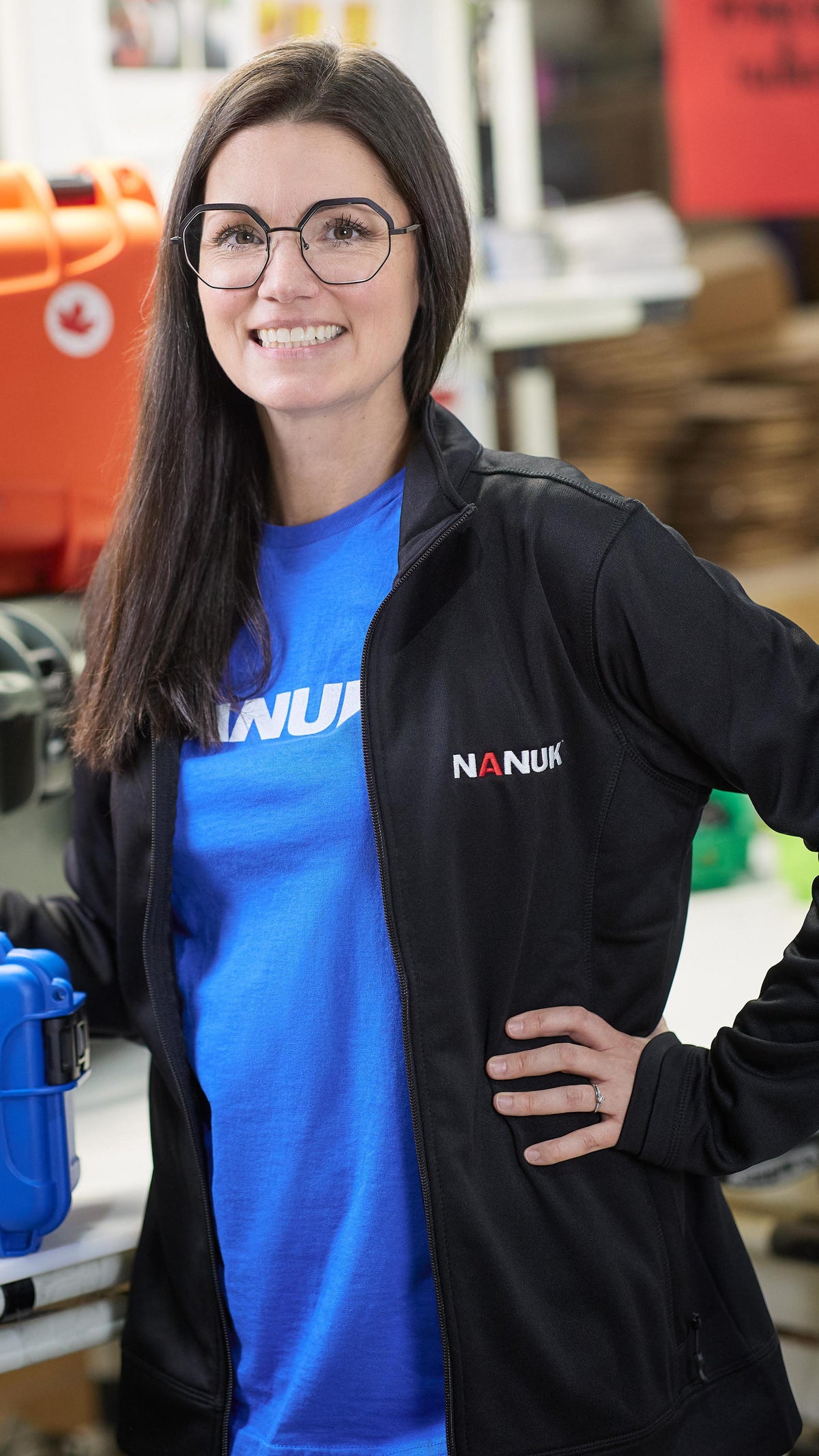 Woman wearing a blue Nanuk shirt and black jacket with a blue case in a workshop setting
