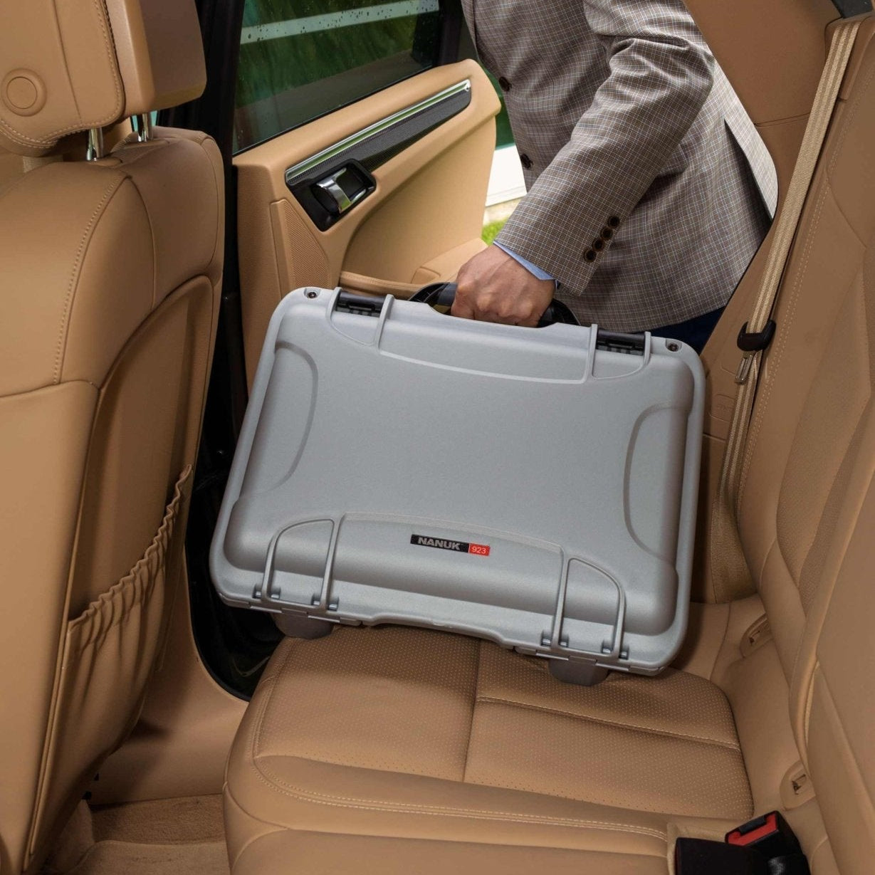 Person loading a large gray suitcase into the back of a car with beige interior.