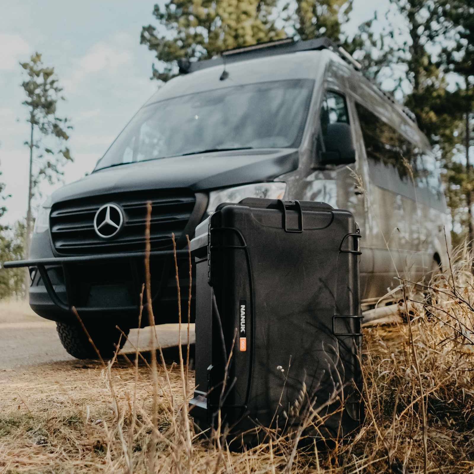 Mercedes-Benz van with a black suitcase in front of it in a natural setting