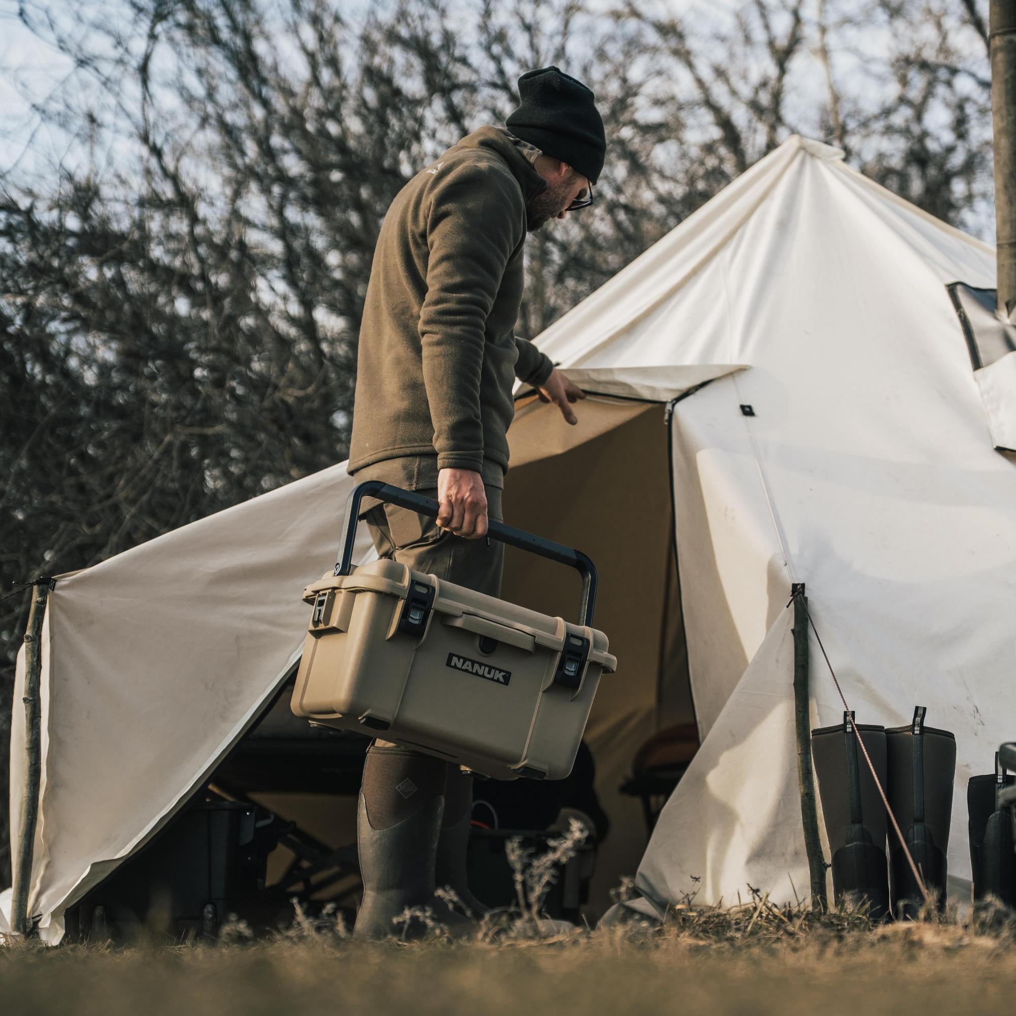 Person holding a cooler near a tent in a camping setting Person holding a cooler near a tent in a camping setting