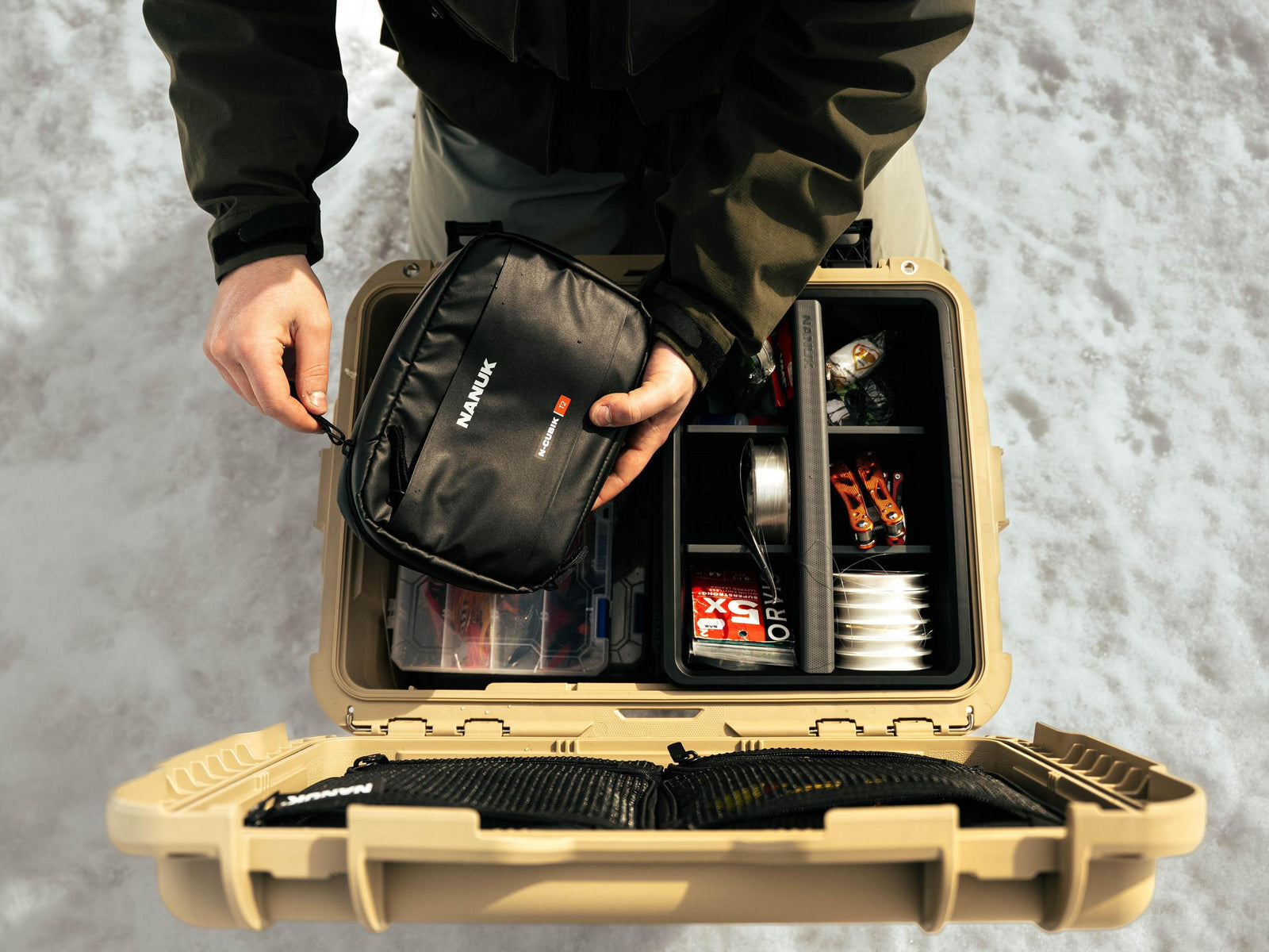 Person opening a beige tackle box filled with fishing gear against a snowy background