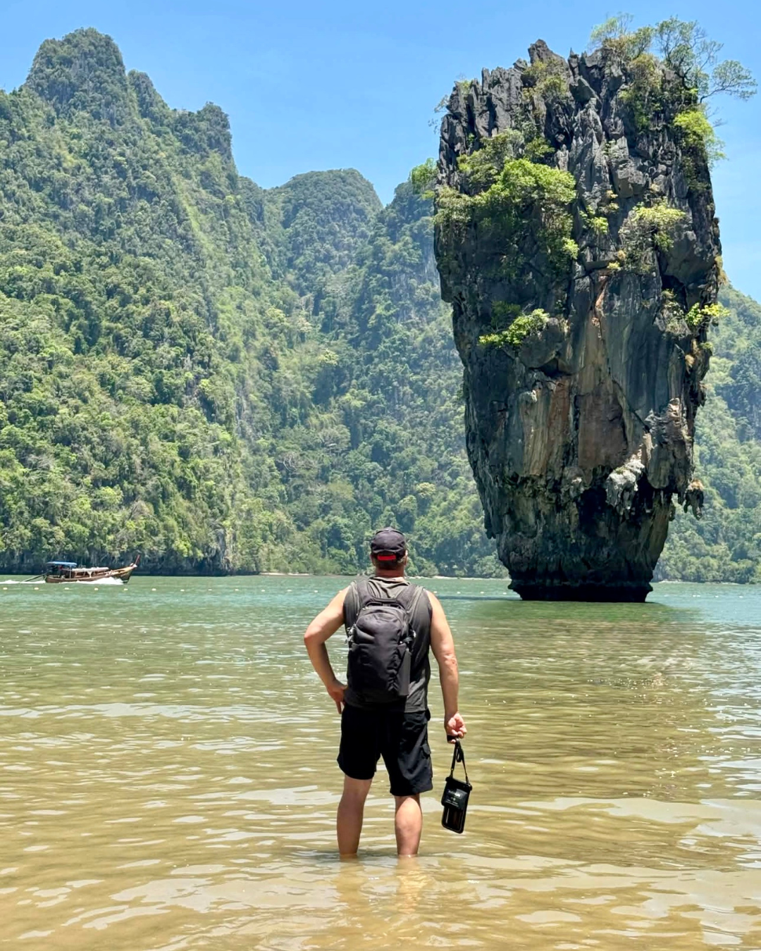 Person standing in water with a scenic rock formation and mountains in the background