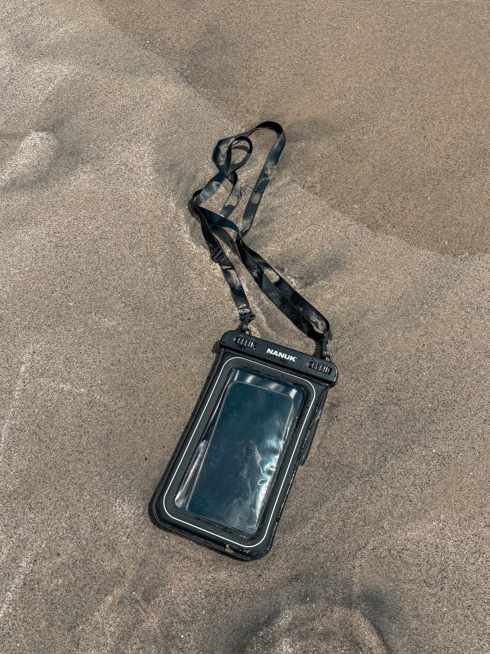 Black phone case with lanyard on sandy surface
