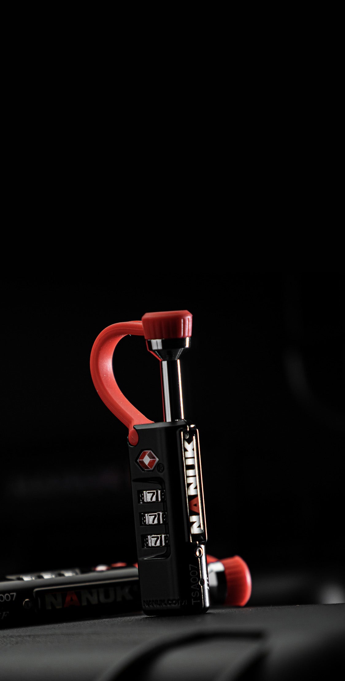 Red and black NANUK TSA-approved padlock with combination dial set on a dark background, emphasizing security and protection for valuable items.