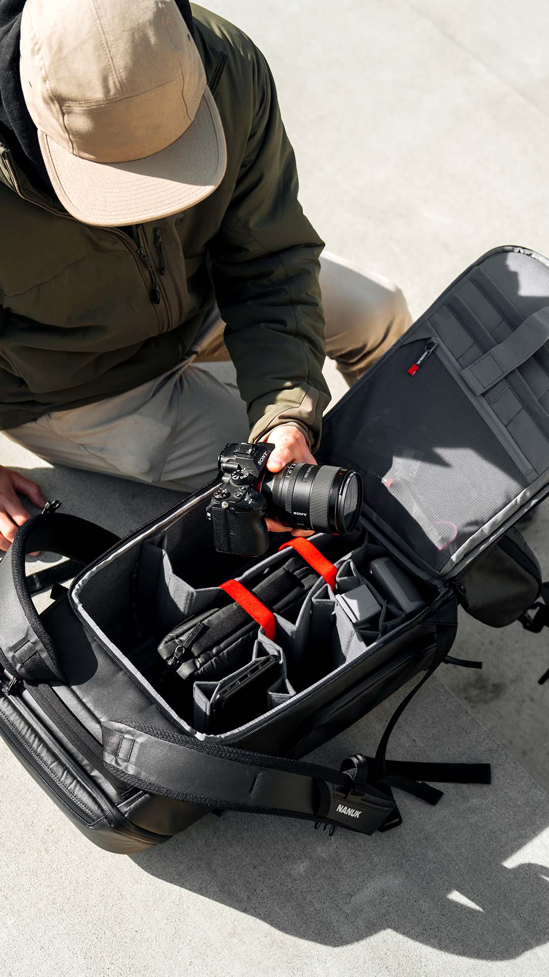 Person opening a black camera bag with a camera inside on a light gray surface.