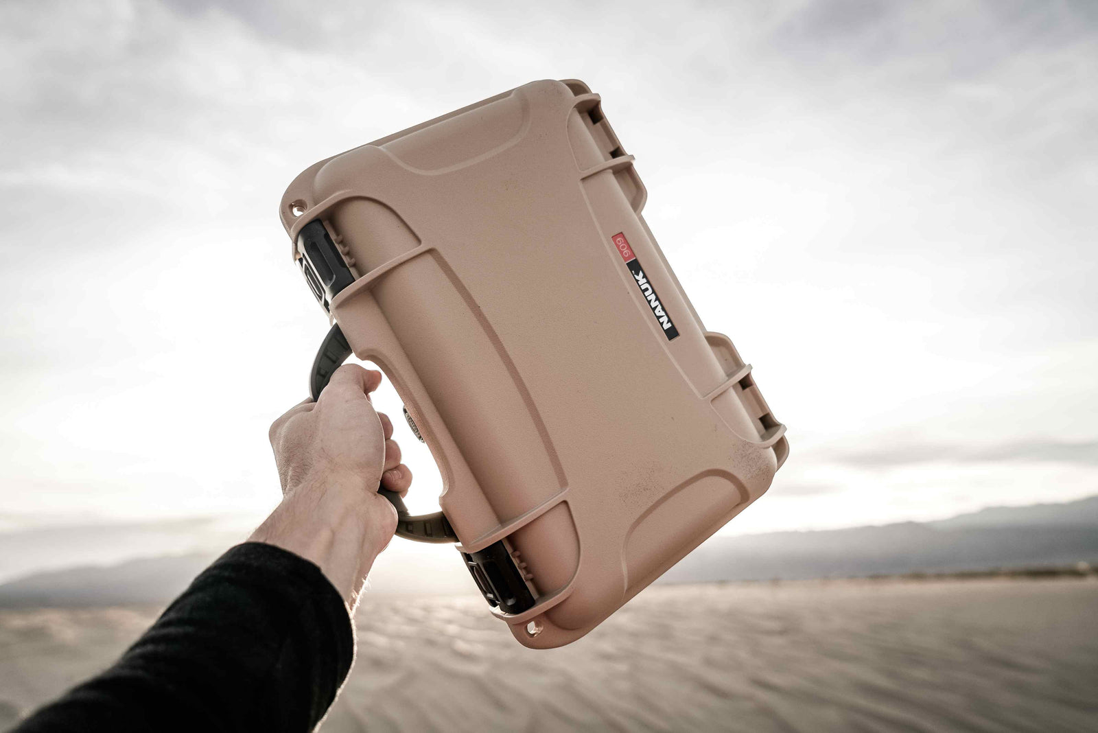 Close-up of a NANUK 909 tan hard case, demonstrating its resilience in a rugged desert setting.