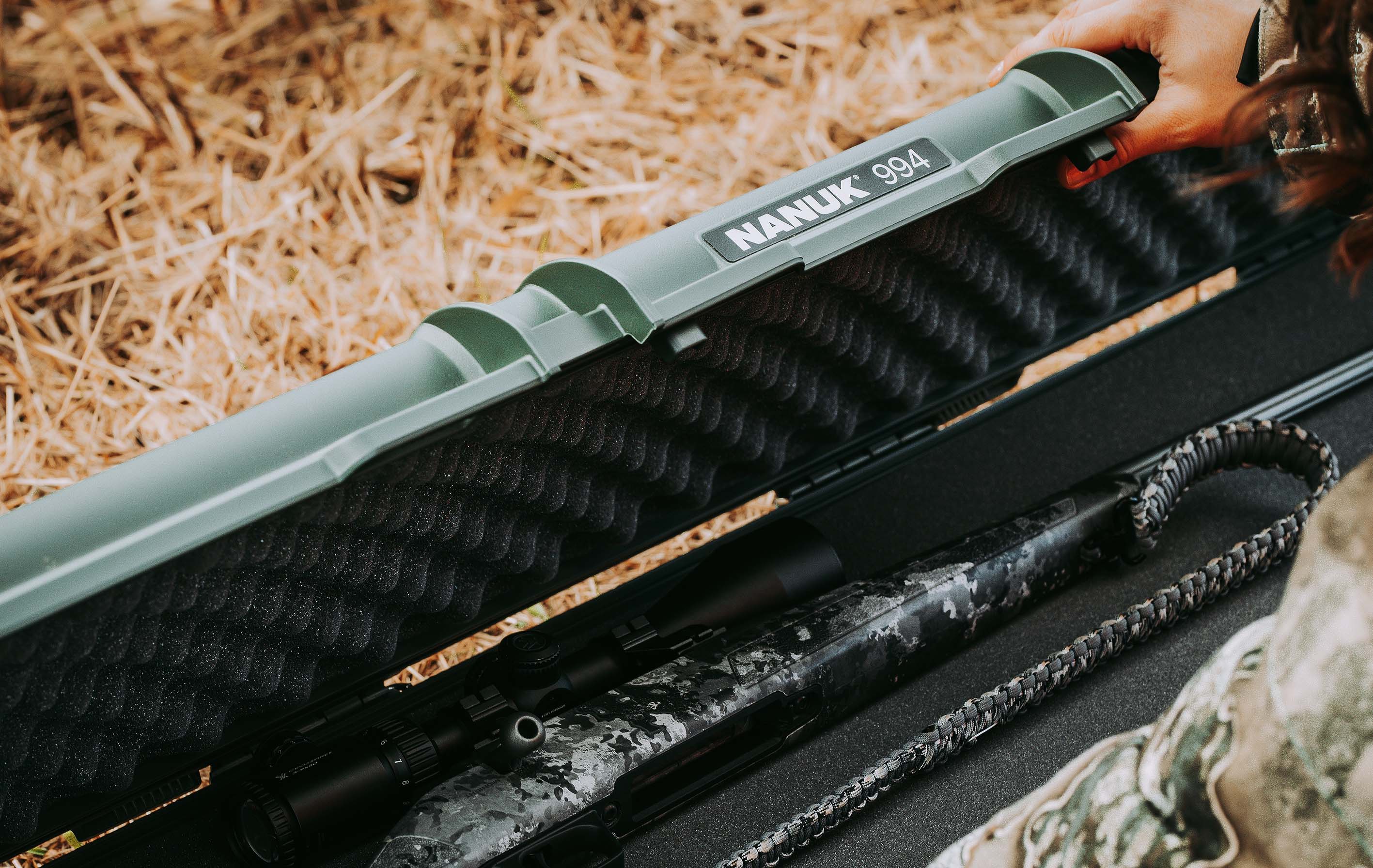 A hand opens a NANUK 994 case, revealing a camouflage hunting rifle and strap nestled in foam, ideal for nanuk cases hunting and outdoor promotion.