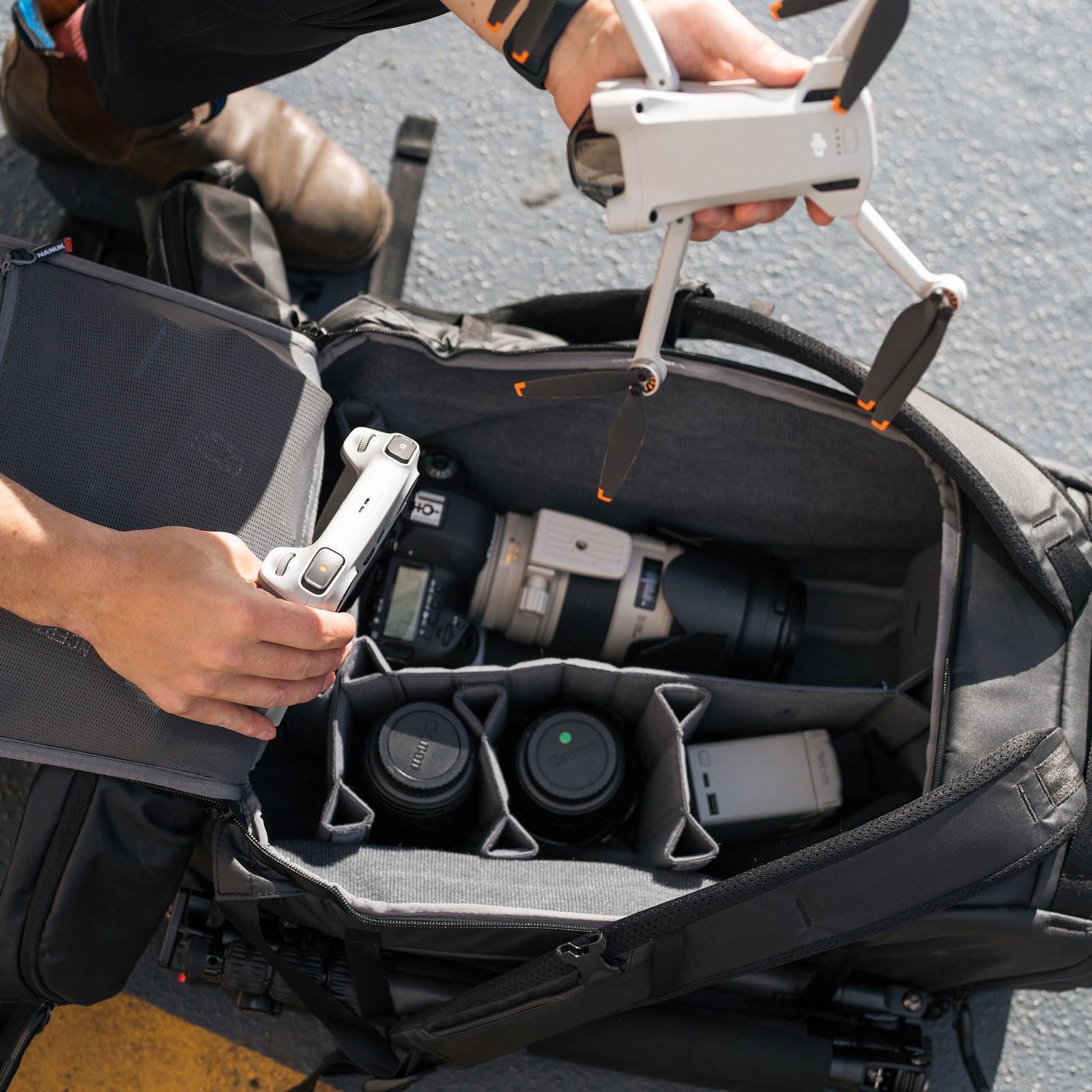 Person organizing camera equipment in a backpack with a drone.