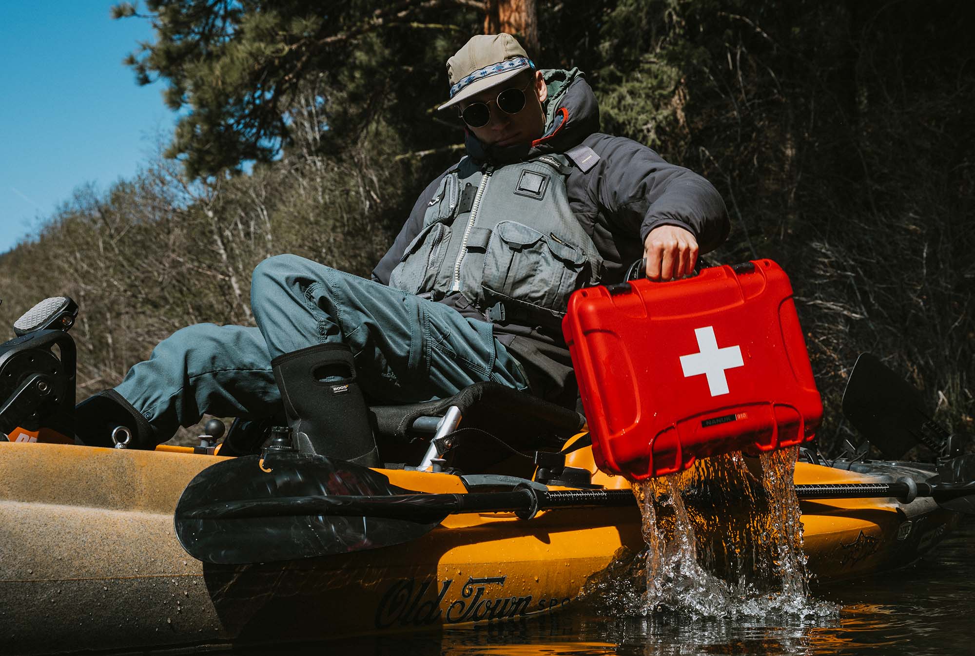 A rugged red NANUK First Aid Case rests on a yellow kayak beside two adventurers preparing for a water journey.