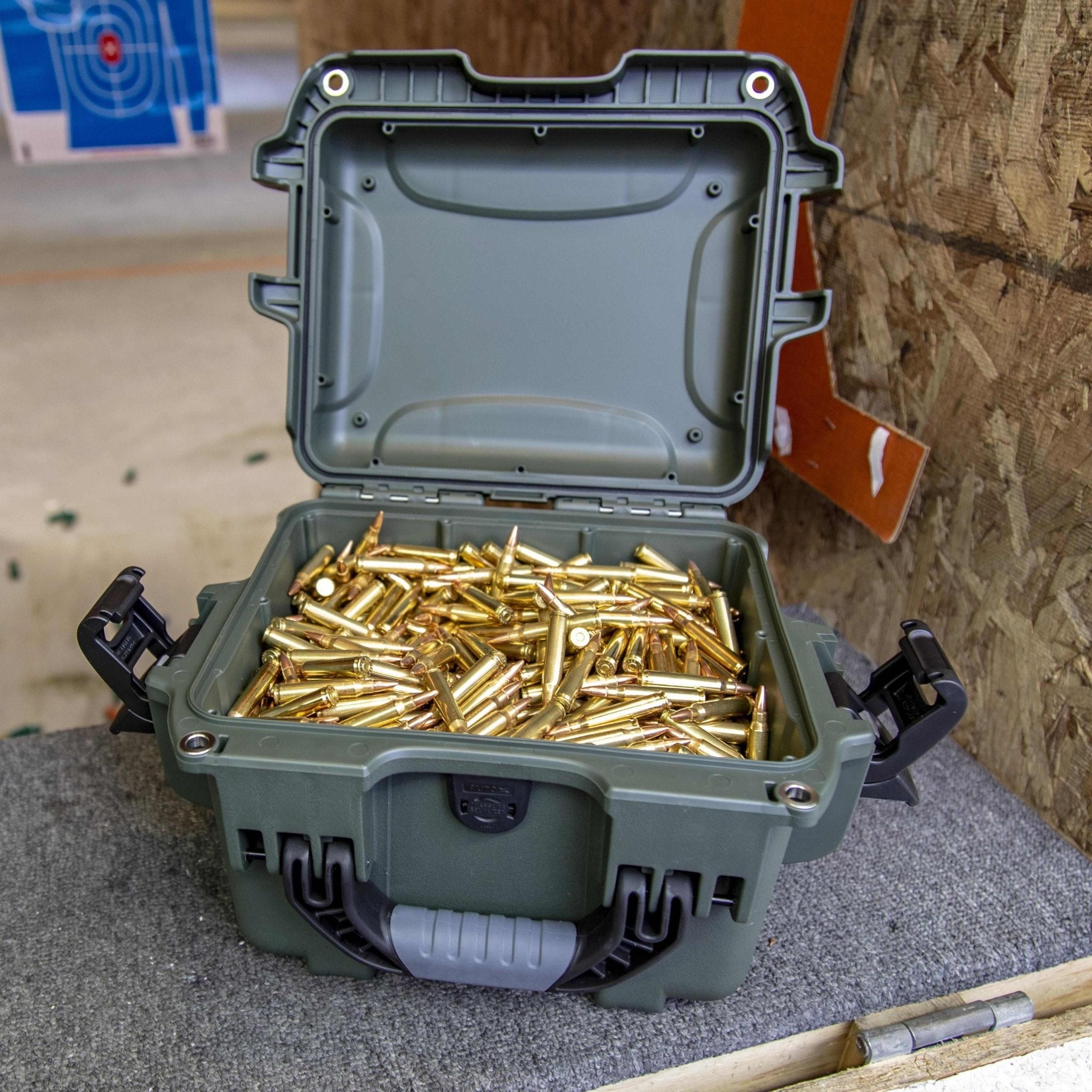 Green ammunition case filled with gold-colored bullets on a gray surface.