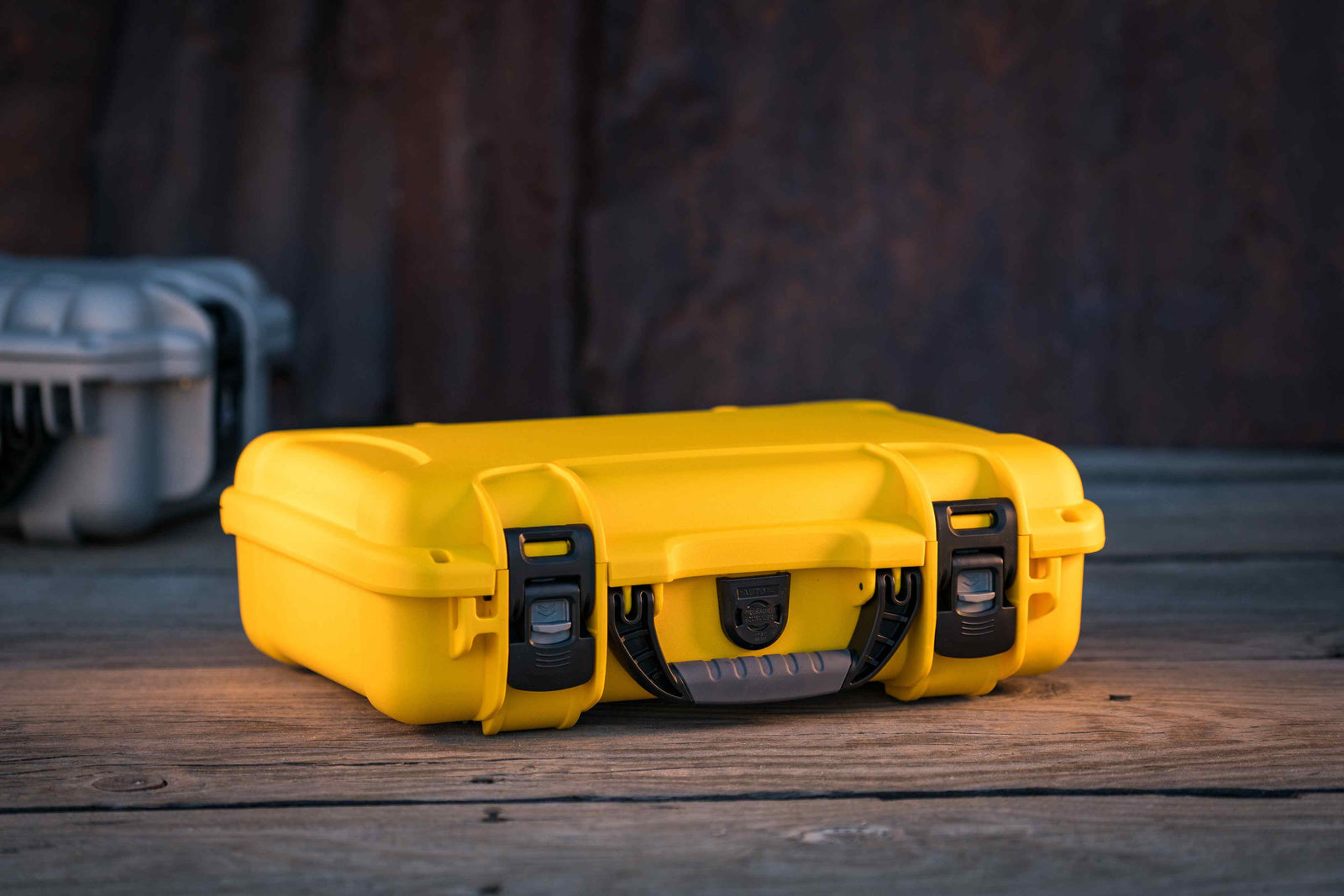The NANUK 910 protective hard case in bright yellow, resting on a textured wooden surface with a rugged industrial backdrop.