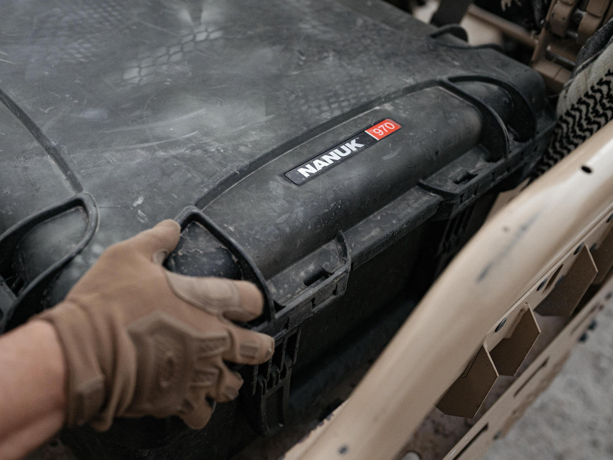 A close-up shot of a person's gloved hand opening a heavy-duty black Nanuk 970 storage case mounted on a vehicle. The case features a prominent black label with the white 'NANUK' brand name and a red 'D10' size badge.
