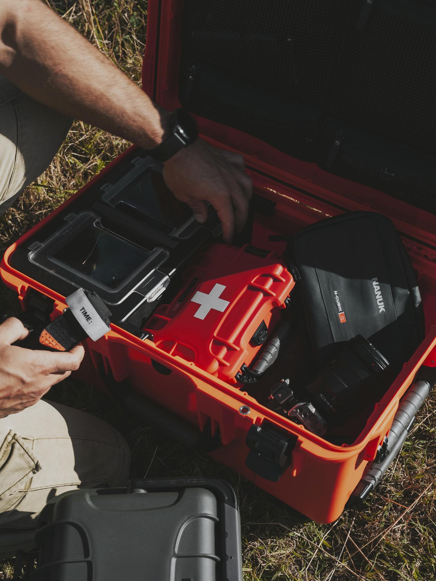 Person organizing items inside a red Pelican case on grass