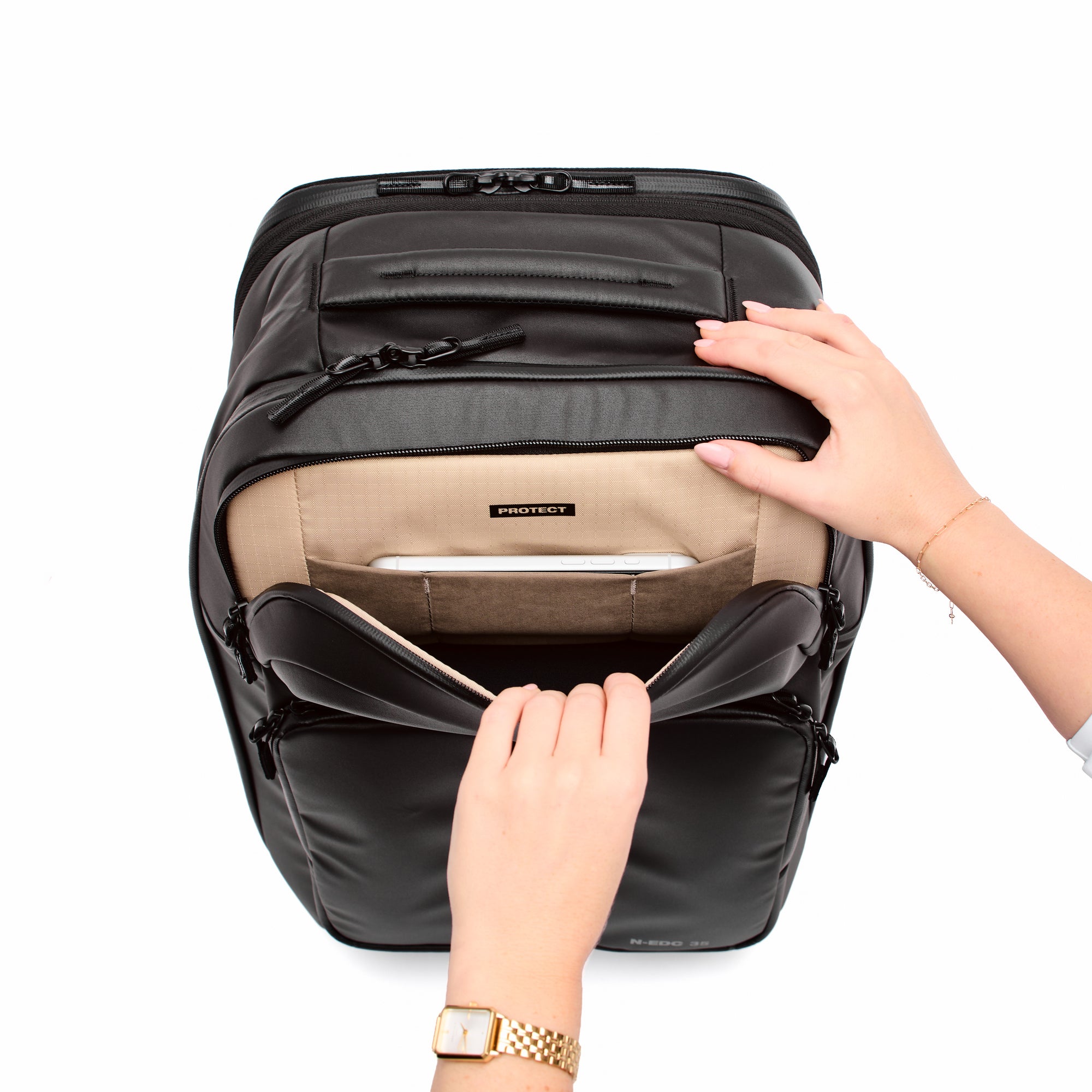 Black backpack with beige interior being adjusted by a hand on a white background