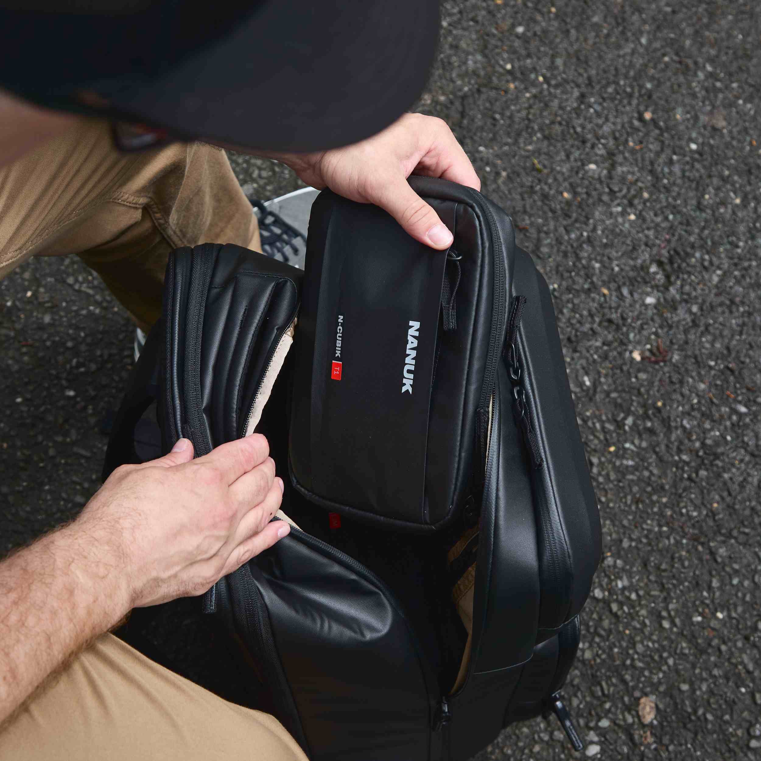 Person holding a black Nanuk backpack with a knife sheath on a textured surface