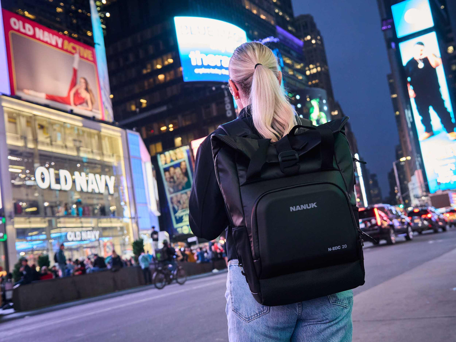 Person with a black backpack walking through a busy city street at night.