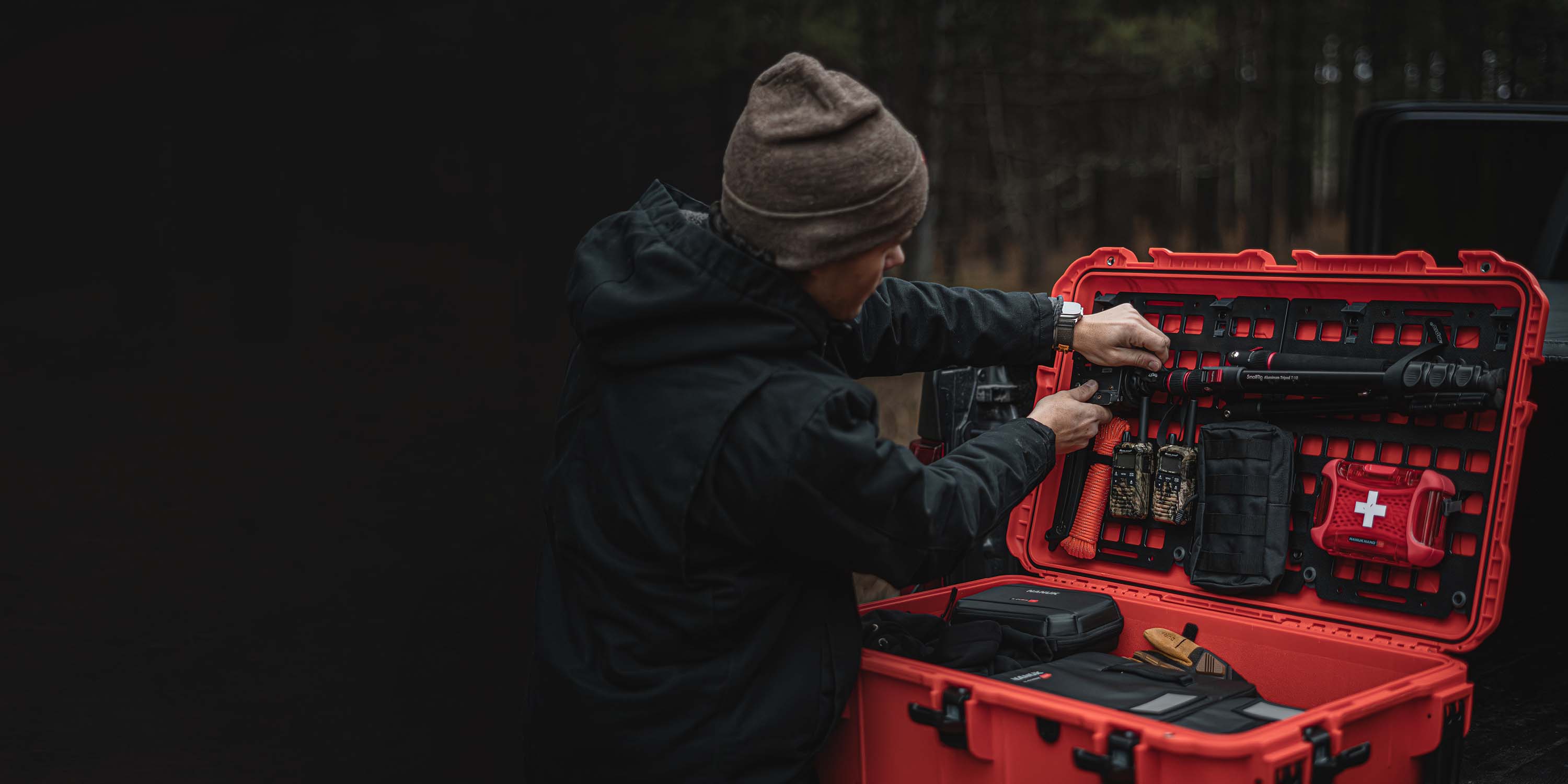 Outdoor enthusiast adjusting tactical gear inside a red NANUK hard case with custom lid organizer and first aid essentials.