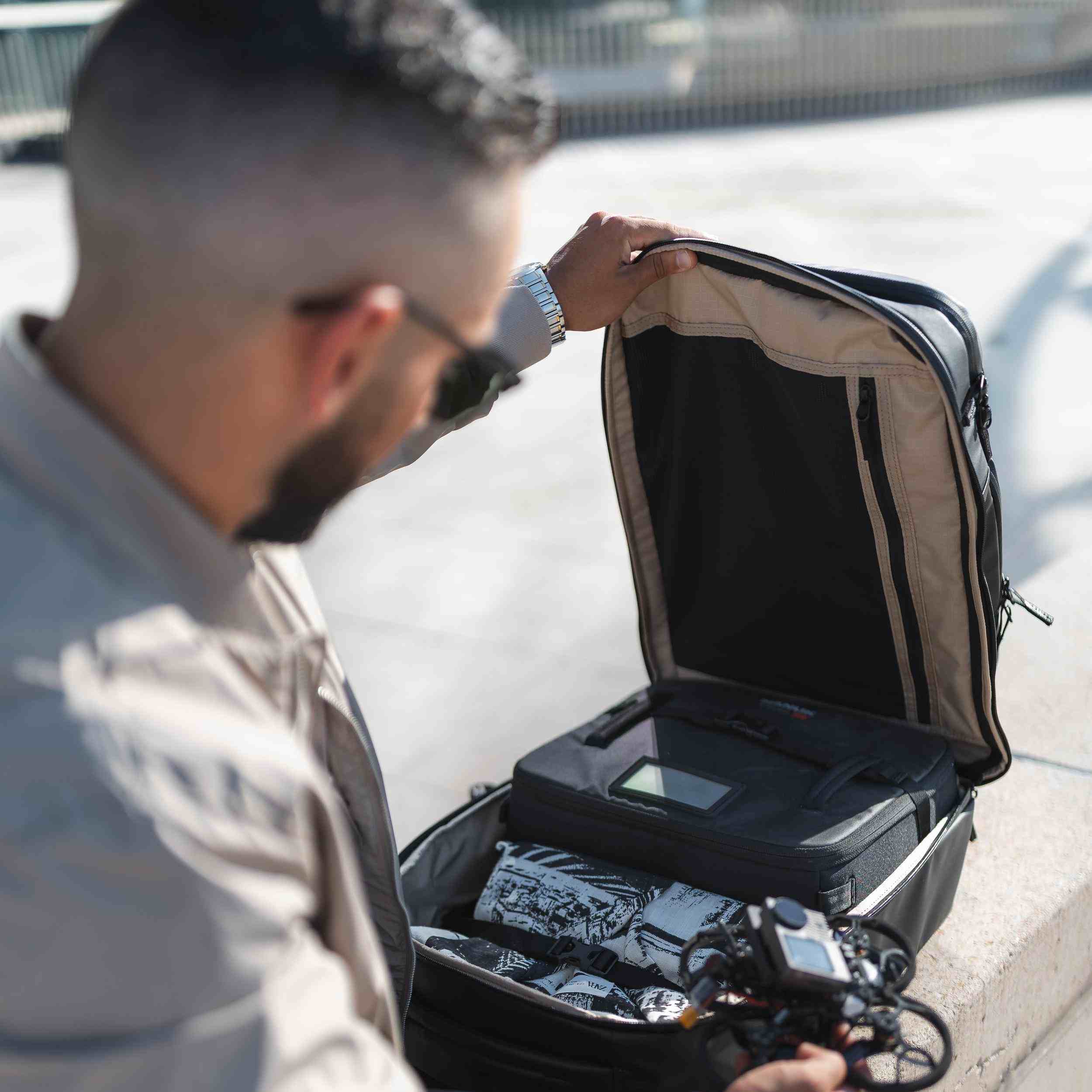 Man opening a suitcase on a sidewalk with electronic equipment inside