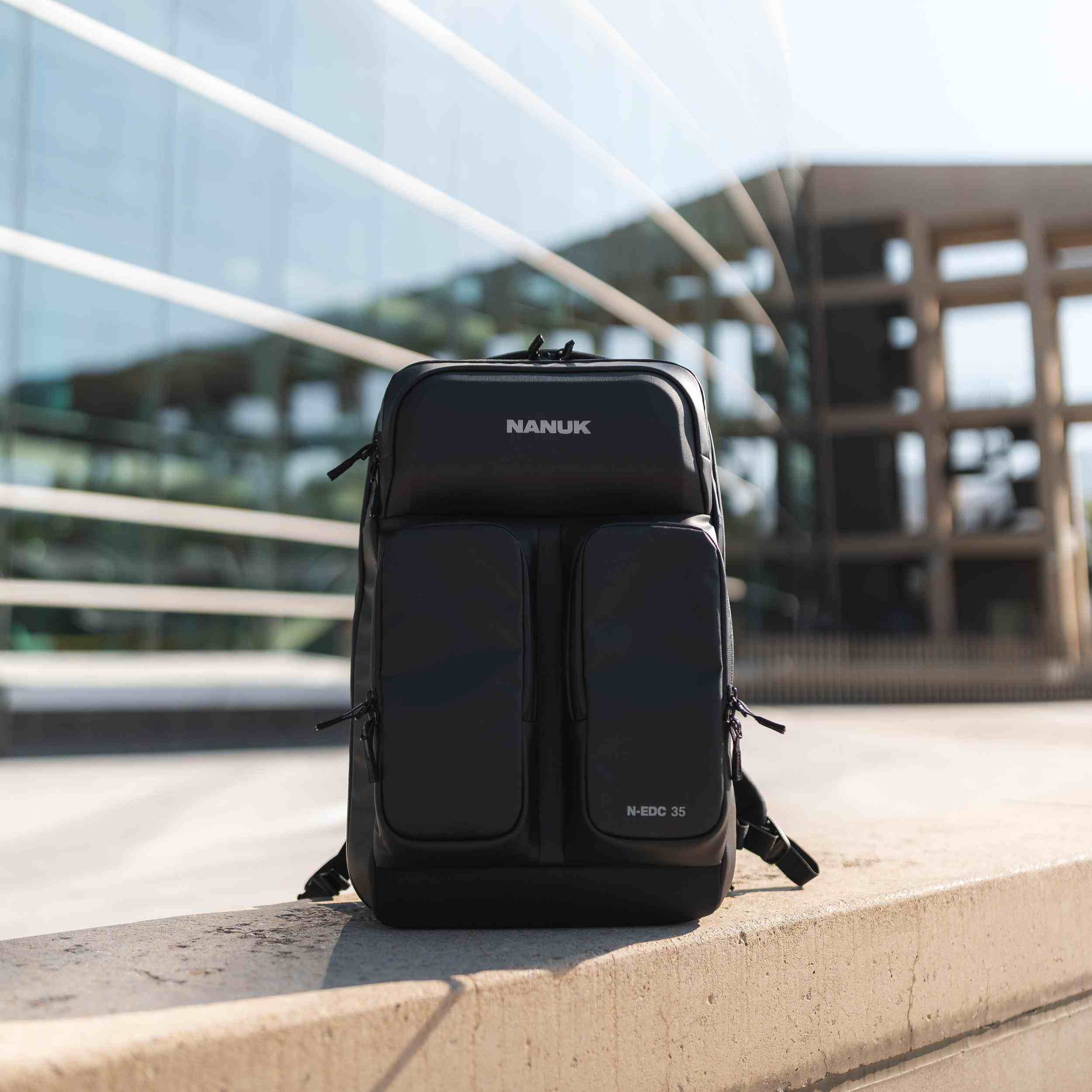 Black backpack with 'NANUK' branding on a concrete ledge with a modern building in the background.