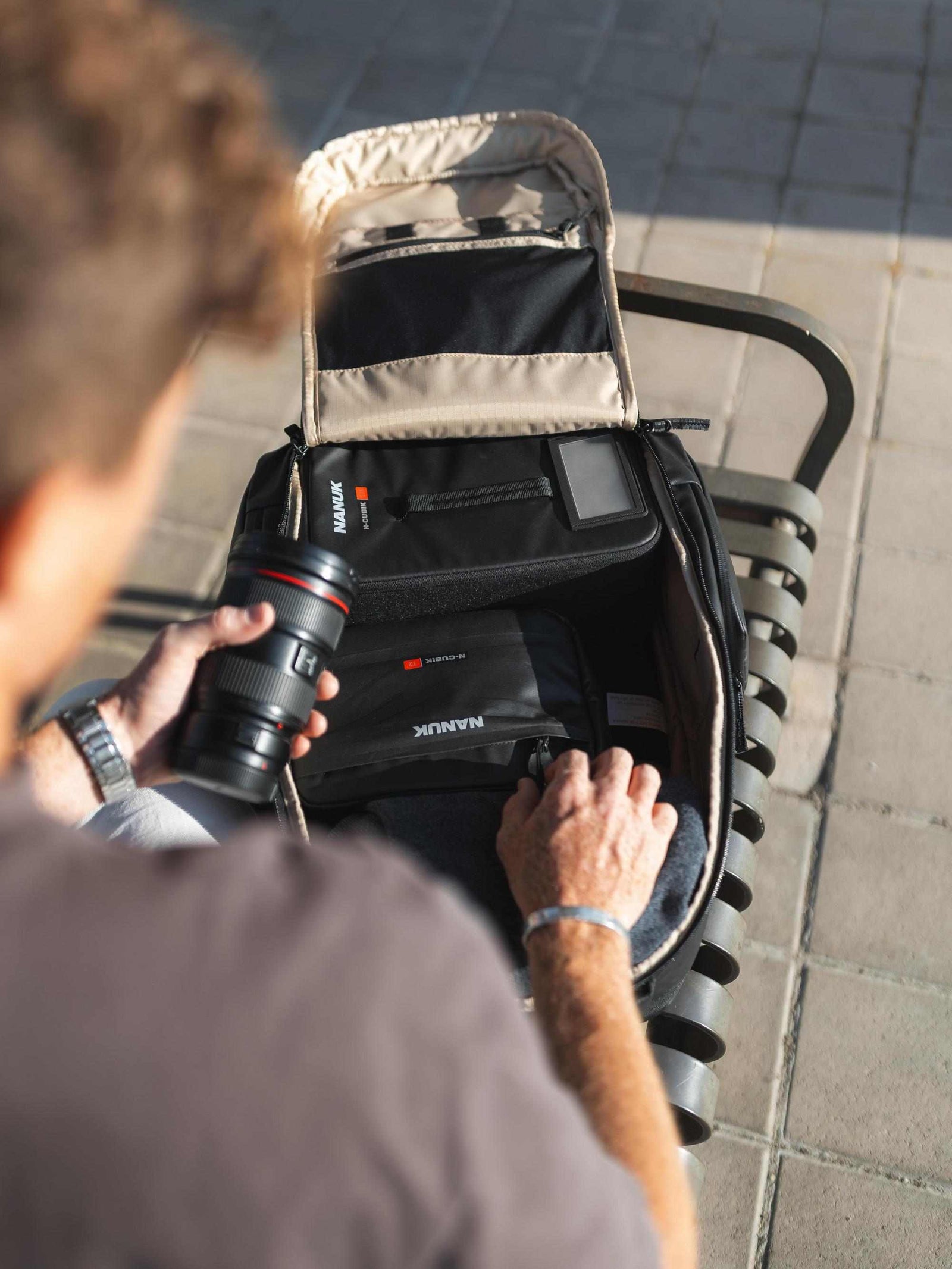 Person organizing camera equipment in a backpack on a tiled floor.