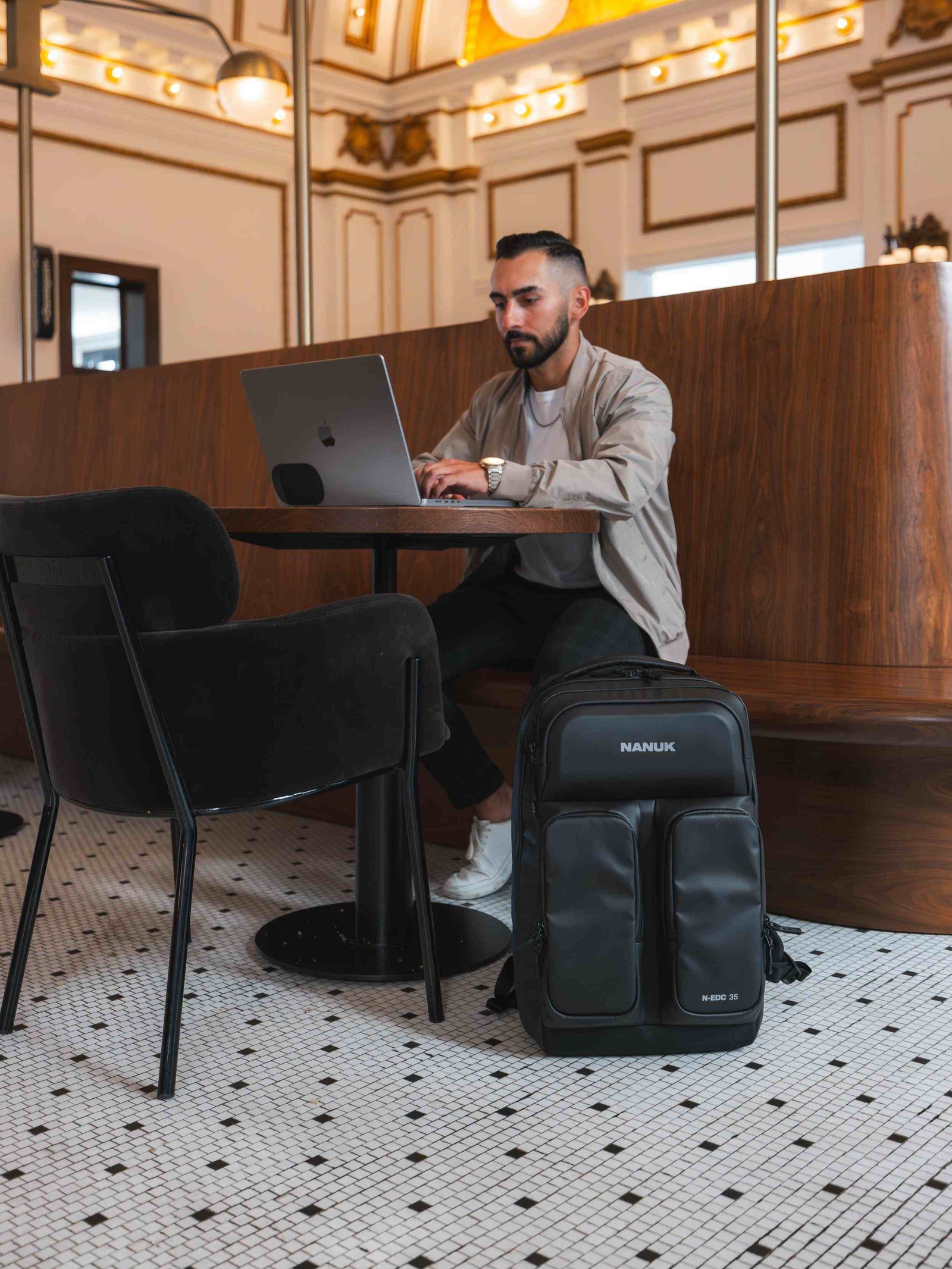 Man using a laptop in a modern cafe with a black backpack on the floor.