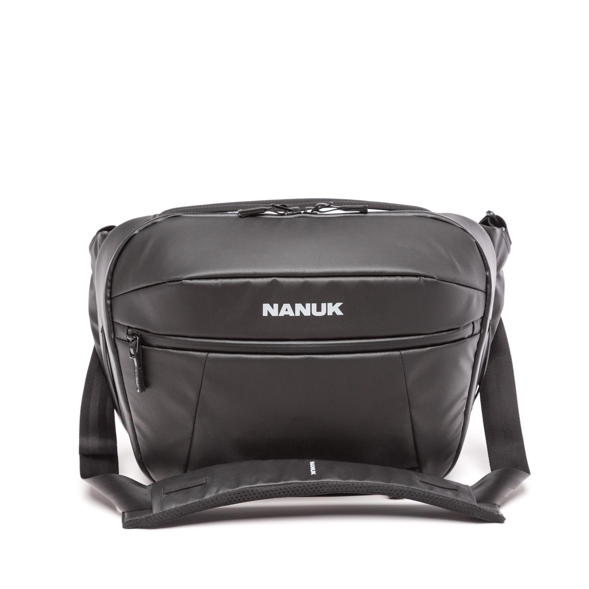 A black Nanuk messenger bag with a front zippered pocket and white brand logo, shown on a clean white background.
