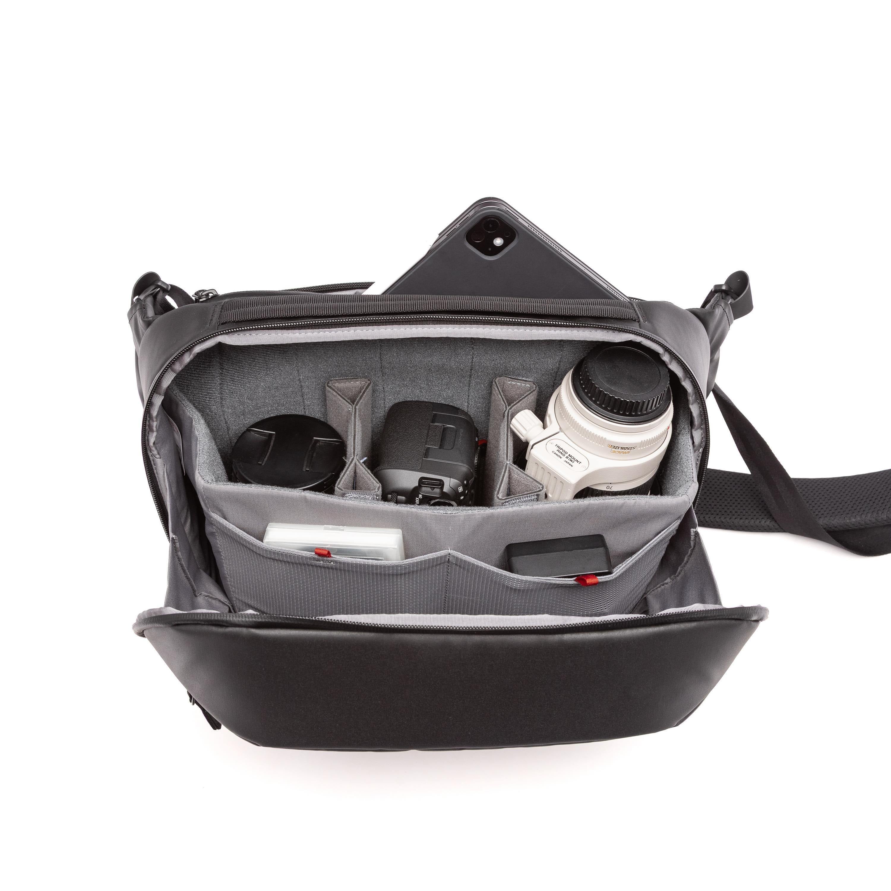 A black and gray camera shoulder bag shown open, filled with camera gear including a lens, camera body, and accessories, on a white background.