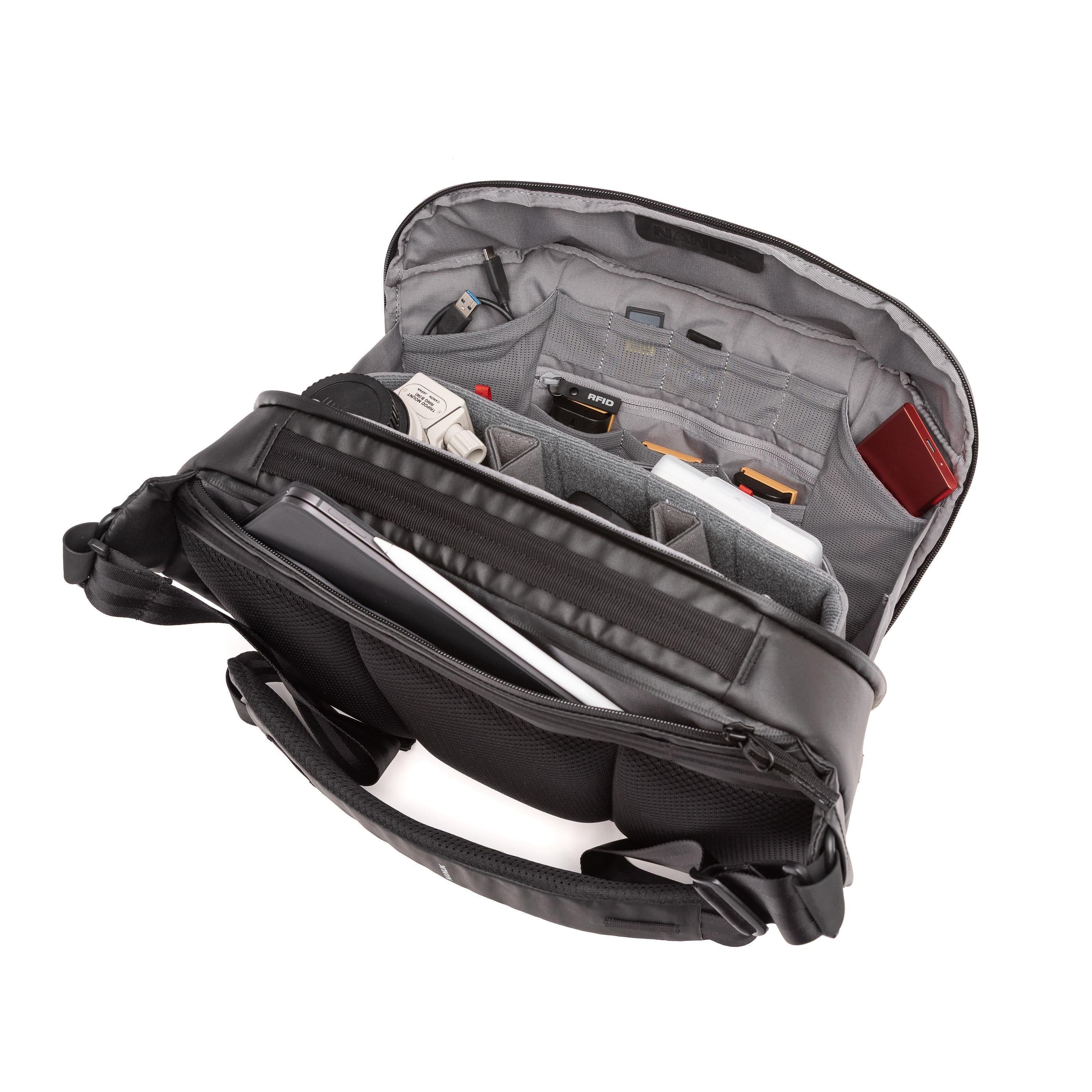 An open black and gray camera shoulder bag shown from a top-down angle, revealing multiple interior compartments, padded pockets, and storage slots filled with camera accessories.