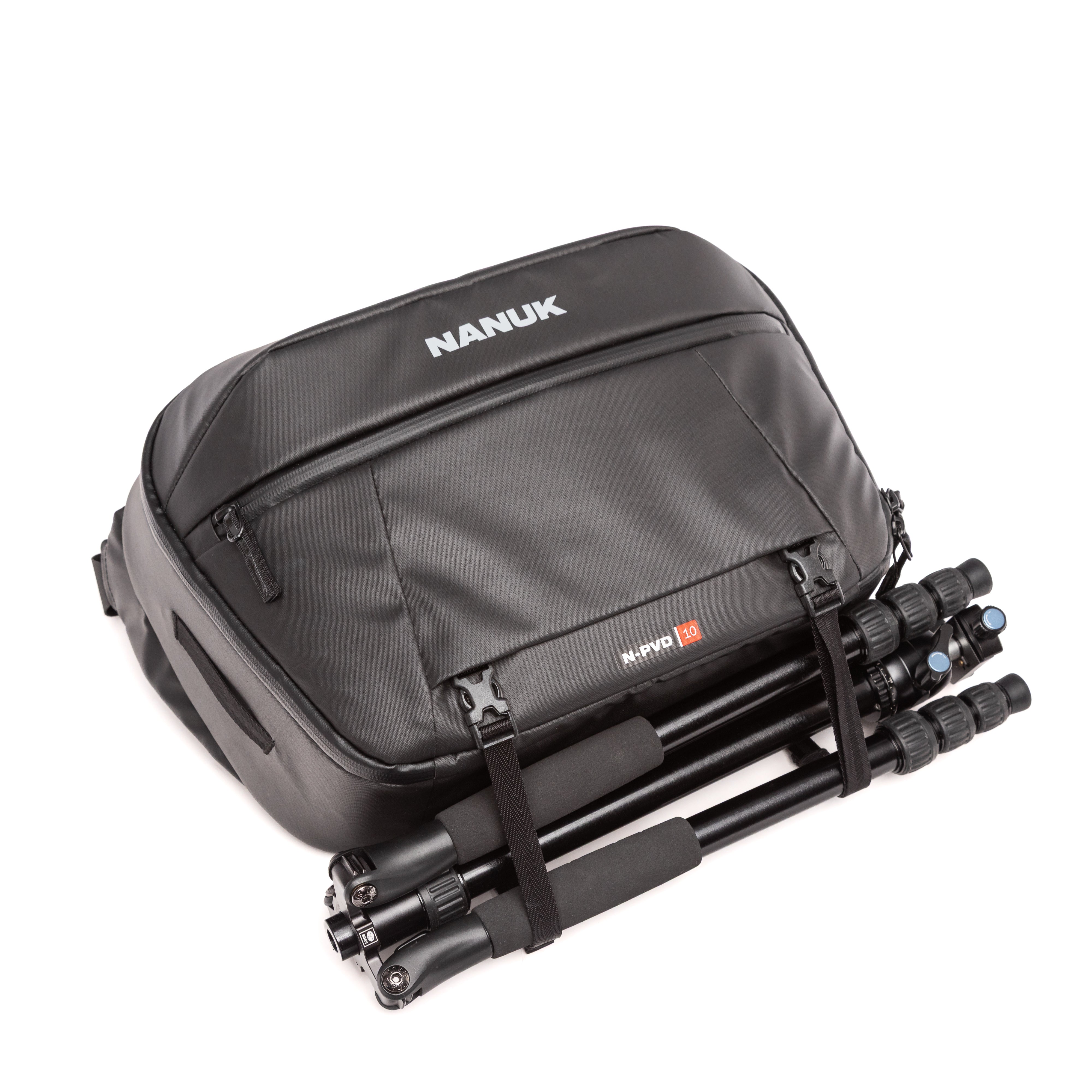 A black Nanuk travel bag with a tripod tucked inside, shown on a clean white background. The bag features the brand name 'NANUK' in white on the front and a small 'NANUK PRO' label on the lower right.