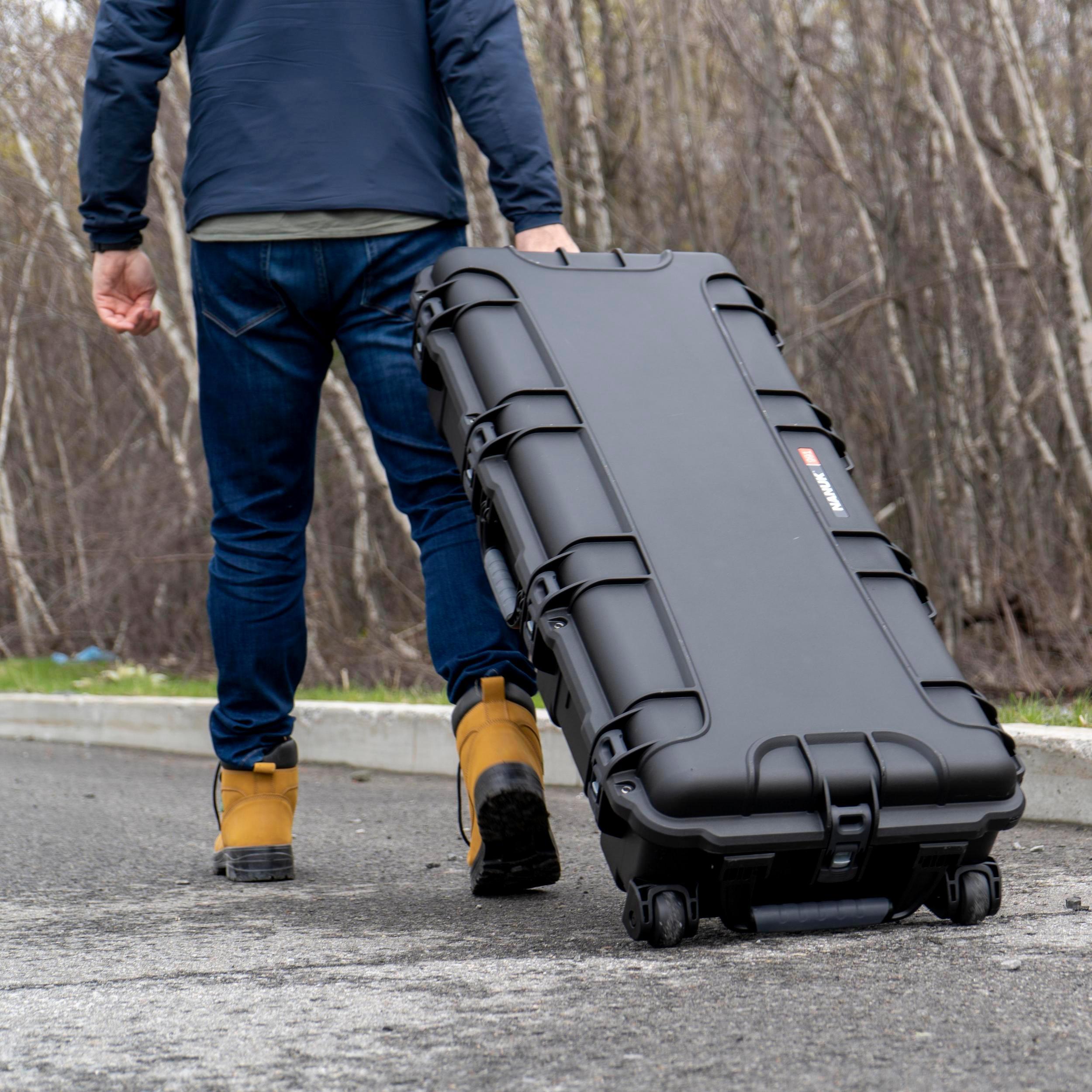 Person carrying a large black suitcase on wheels outdoors.