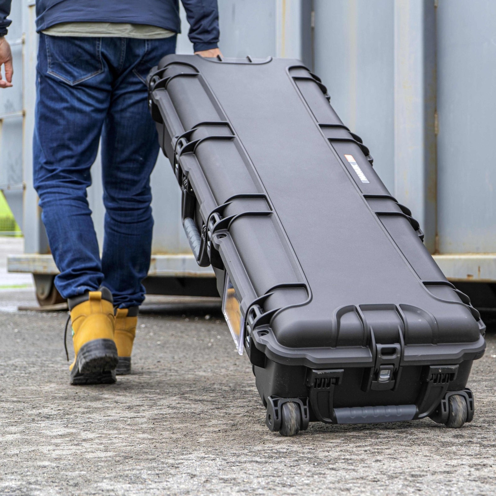 Person walking with a large black hard-shell case outdoors.