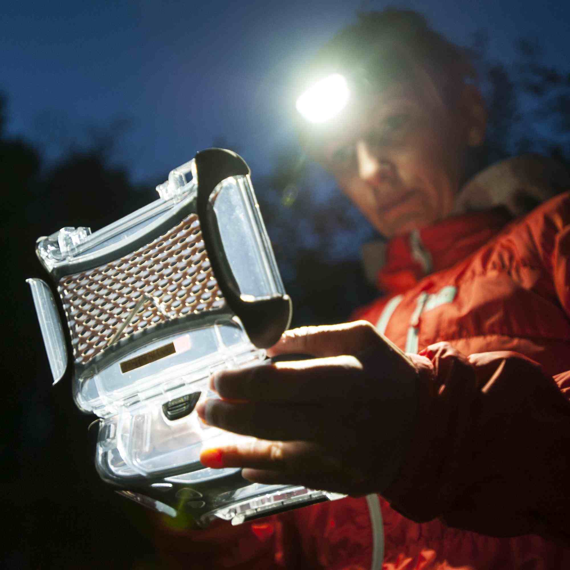 Person holding a clear container with a textured lid at night, illuminated by a flashlight.