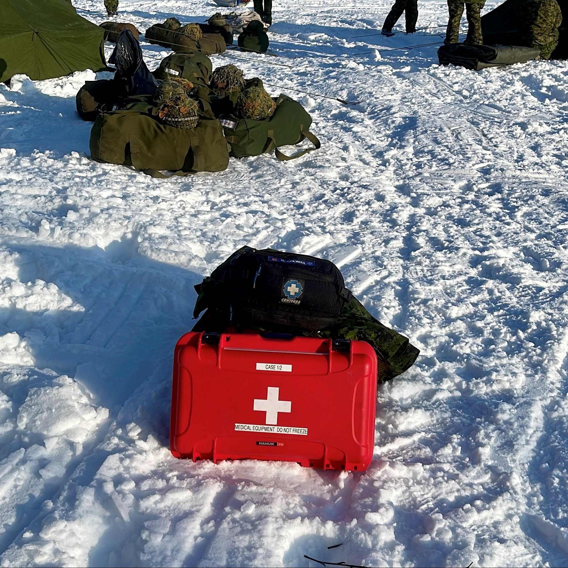 Red medical kit on a snowy ground with people in winter gear in the background.