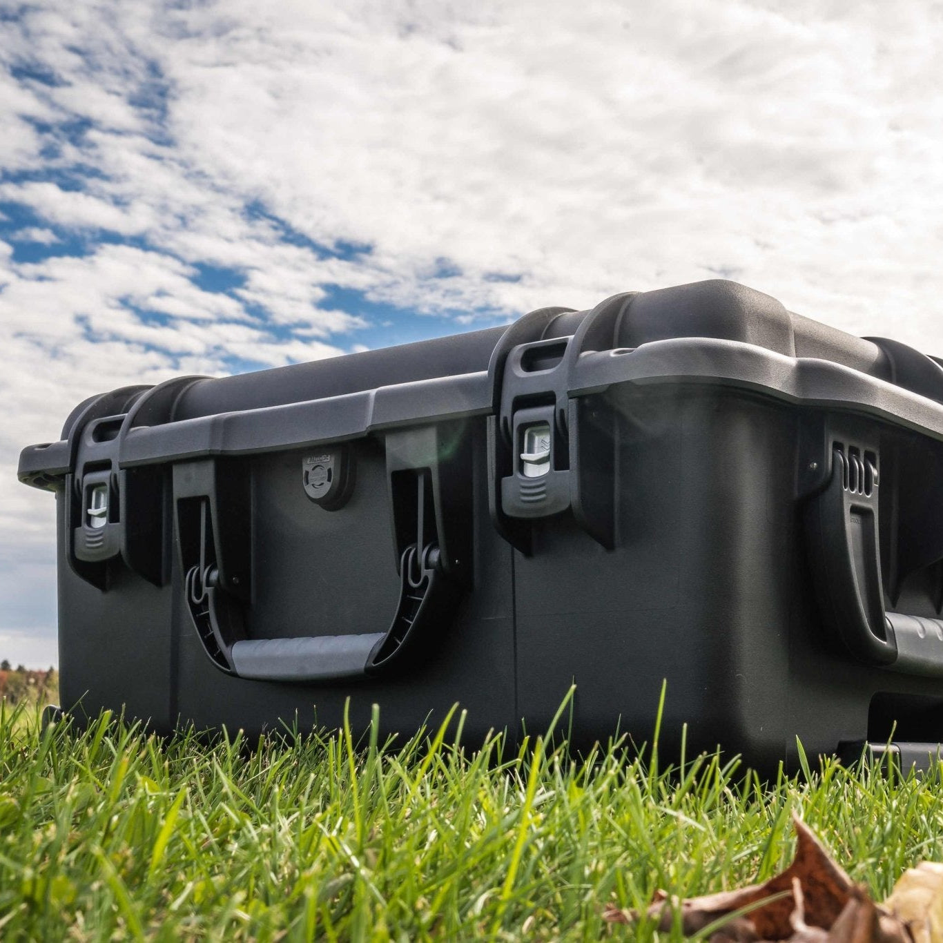 Black hard-shell case on grass with a cloudy sky background