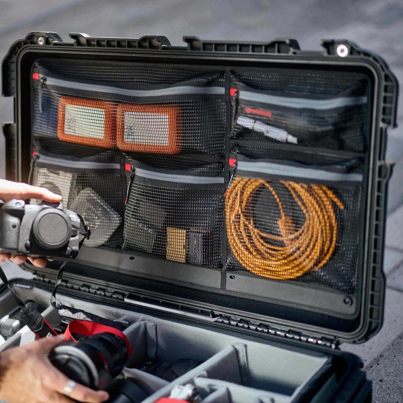 Person holding a camera next to an open black travel case with compartments.